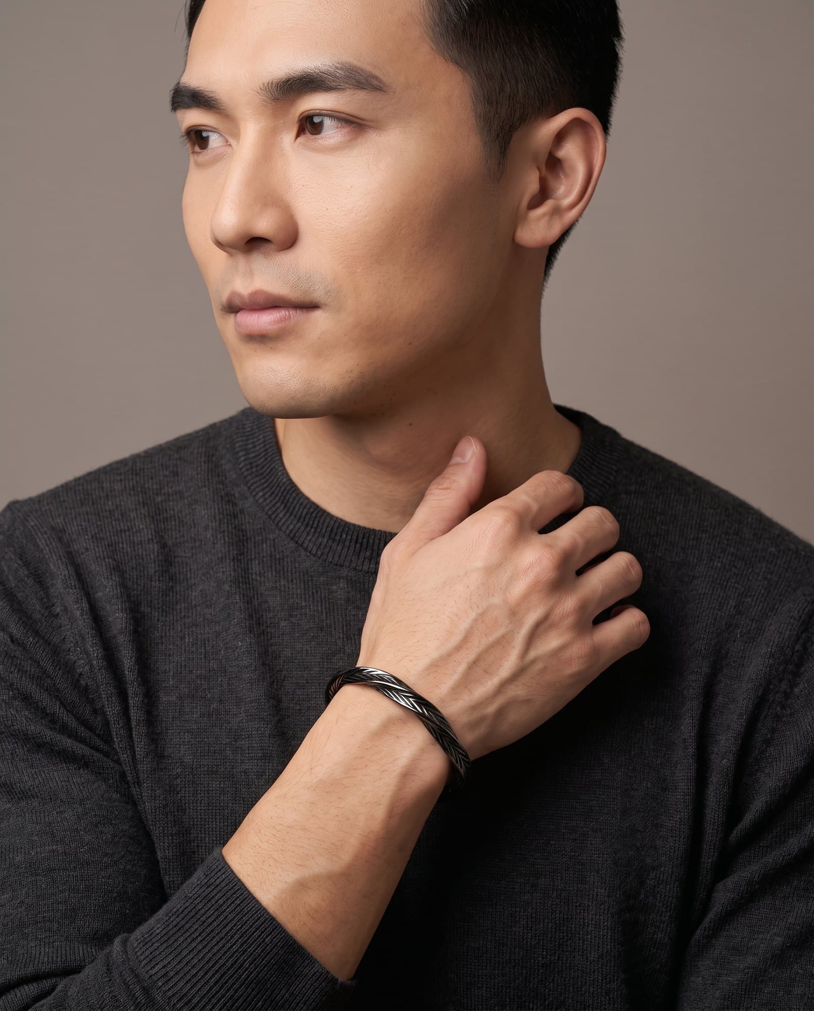 A man in a charcoal knit with his hand at his collarbone, the Amun Chevron Cuff on his wrist.