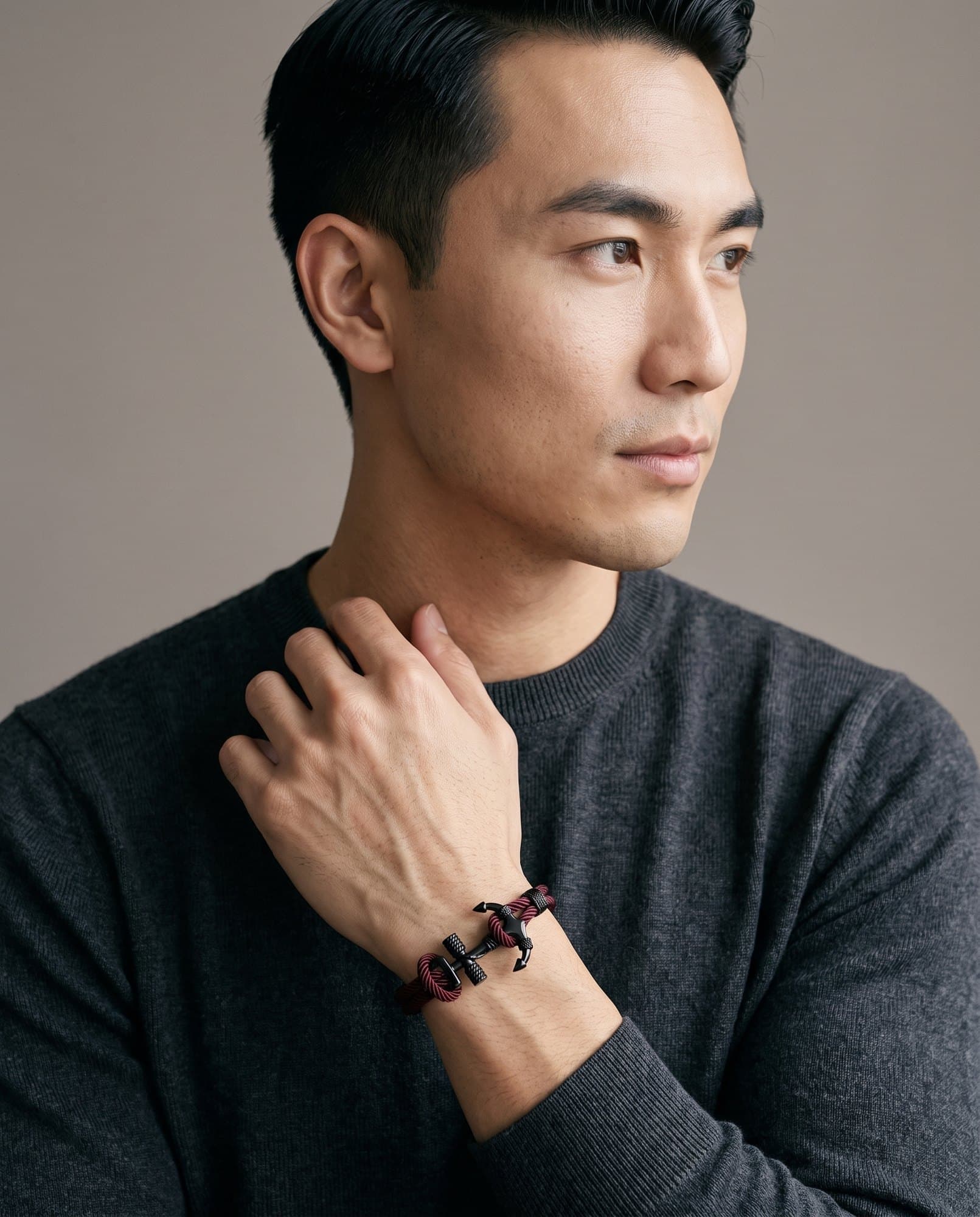 A man in a charcoal knit with his hand at his collarbone, the Anchor Wrap on his wrist.