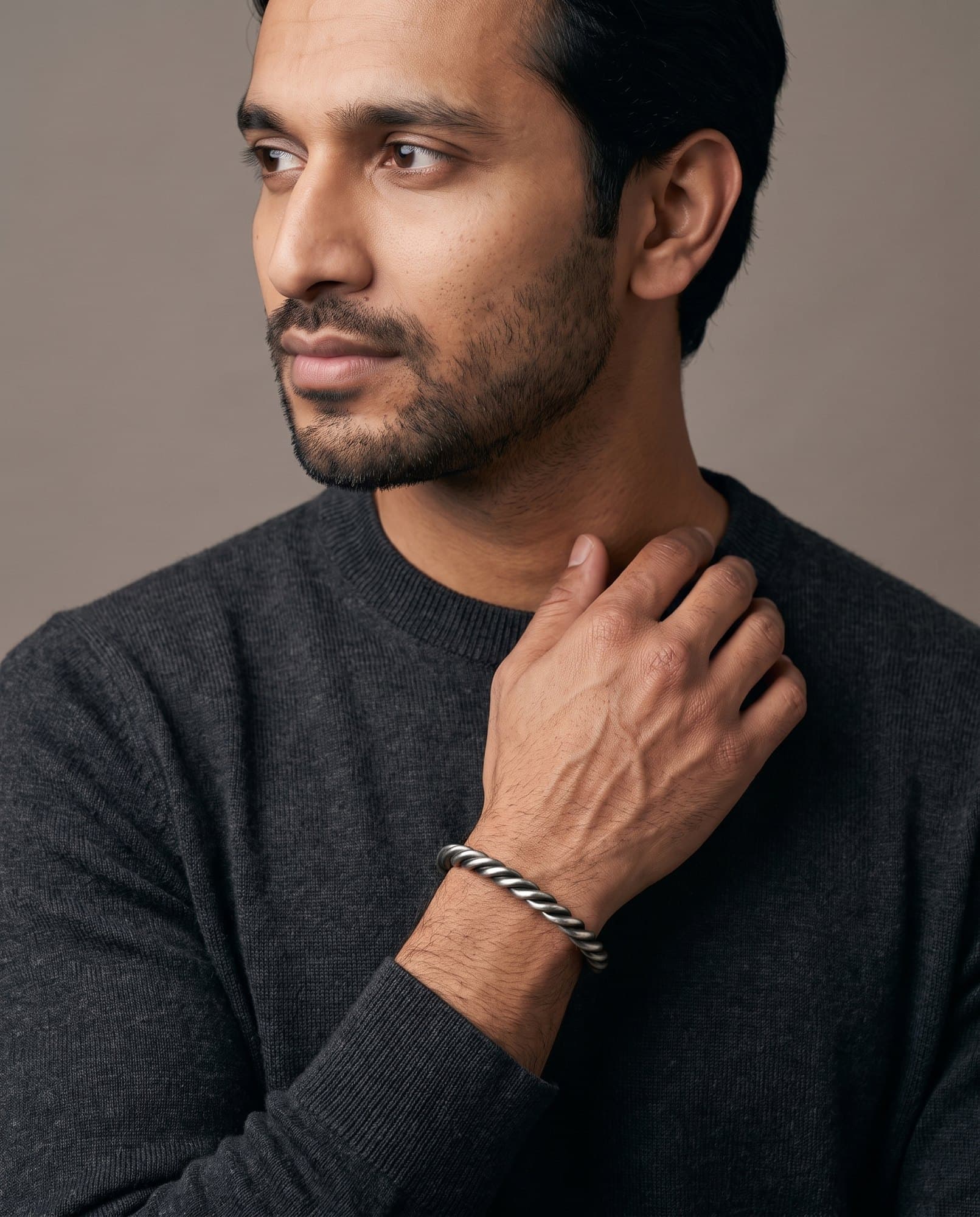 A man in a charcoal knit with his hand at his collarbone, the Cairo Rope Cuff on his wrist.