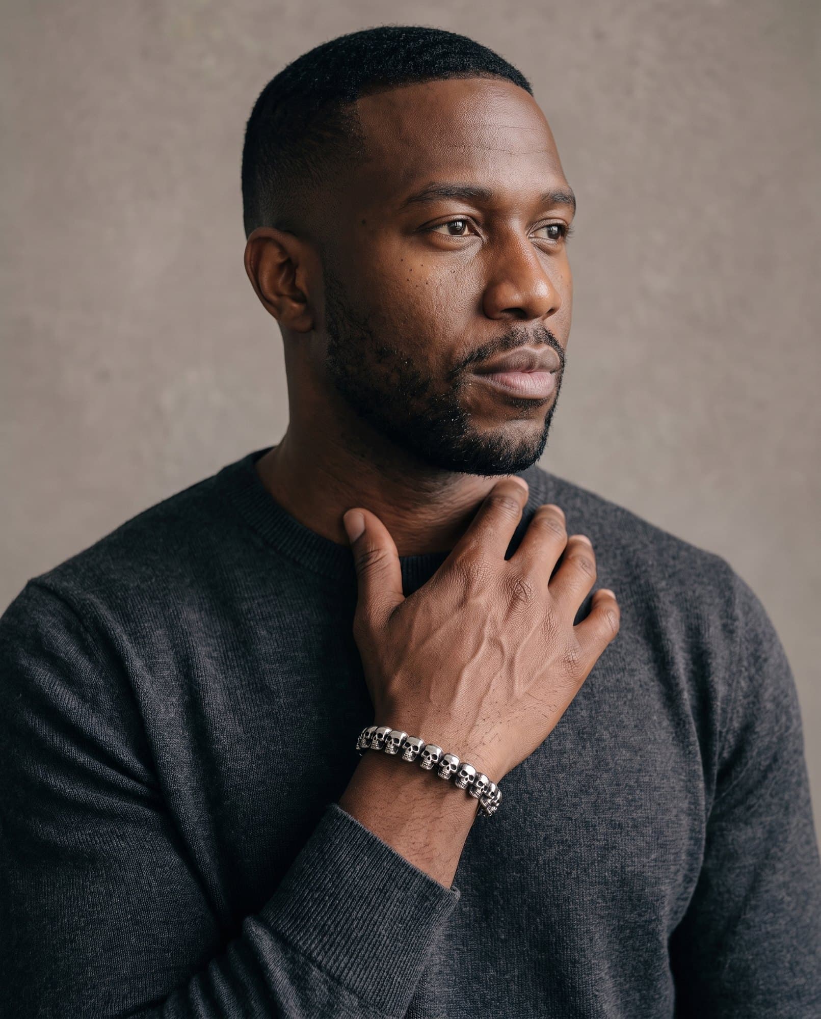 A man in a charcoal knit with his hand at his collarbone, the Cartouche Bead Cuff on his wrist.
