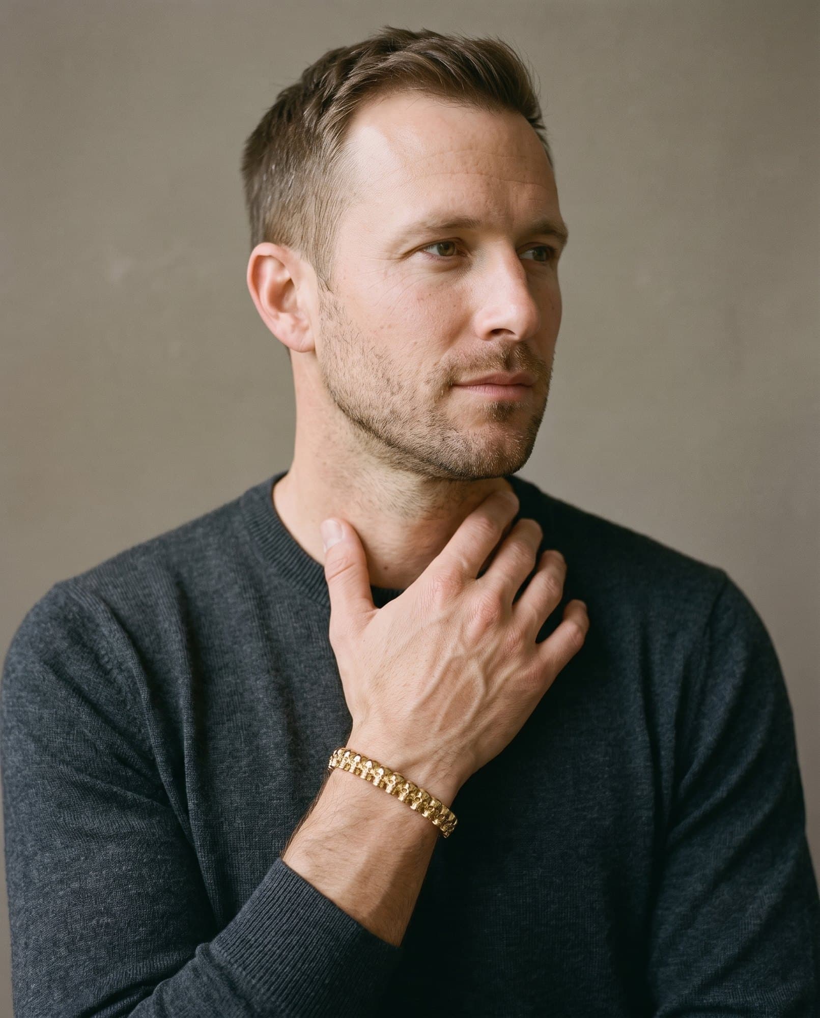 A man in a charcoal knit with his hand at his collarbone, the Cartouche Bead Cuff Gold on his wrist.