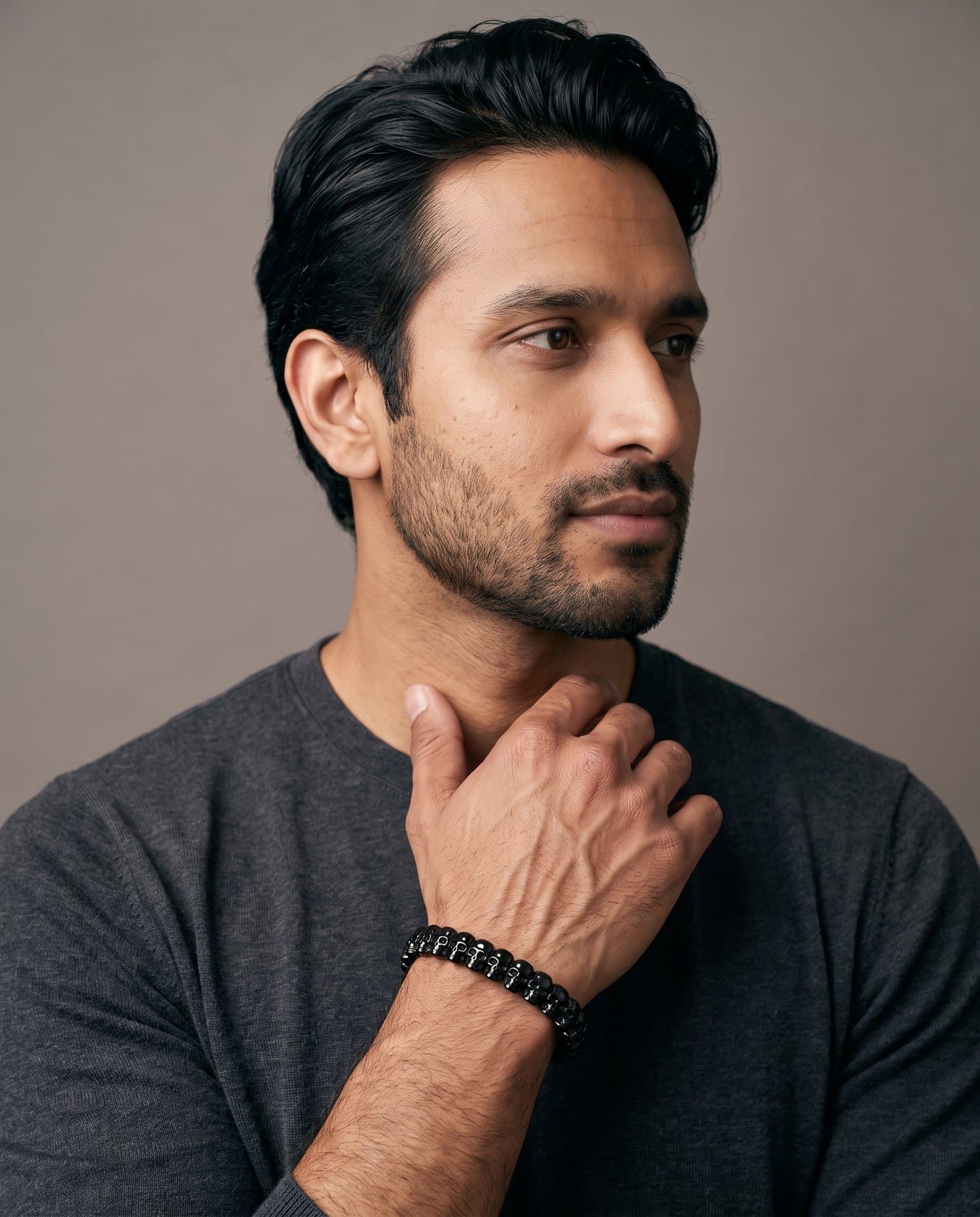 A man in a charcoal knit with his hand at his collarbone, the Cartouche Bead Cuff Noir on his wrist.