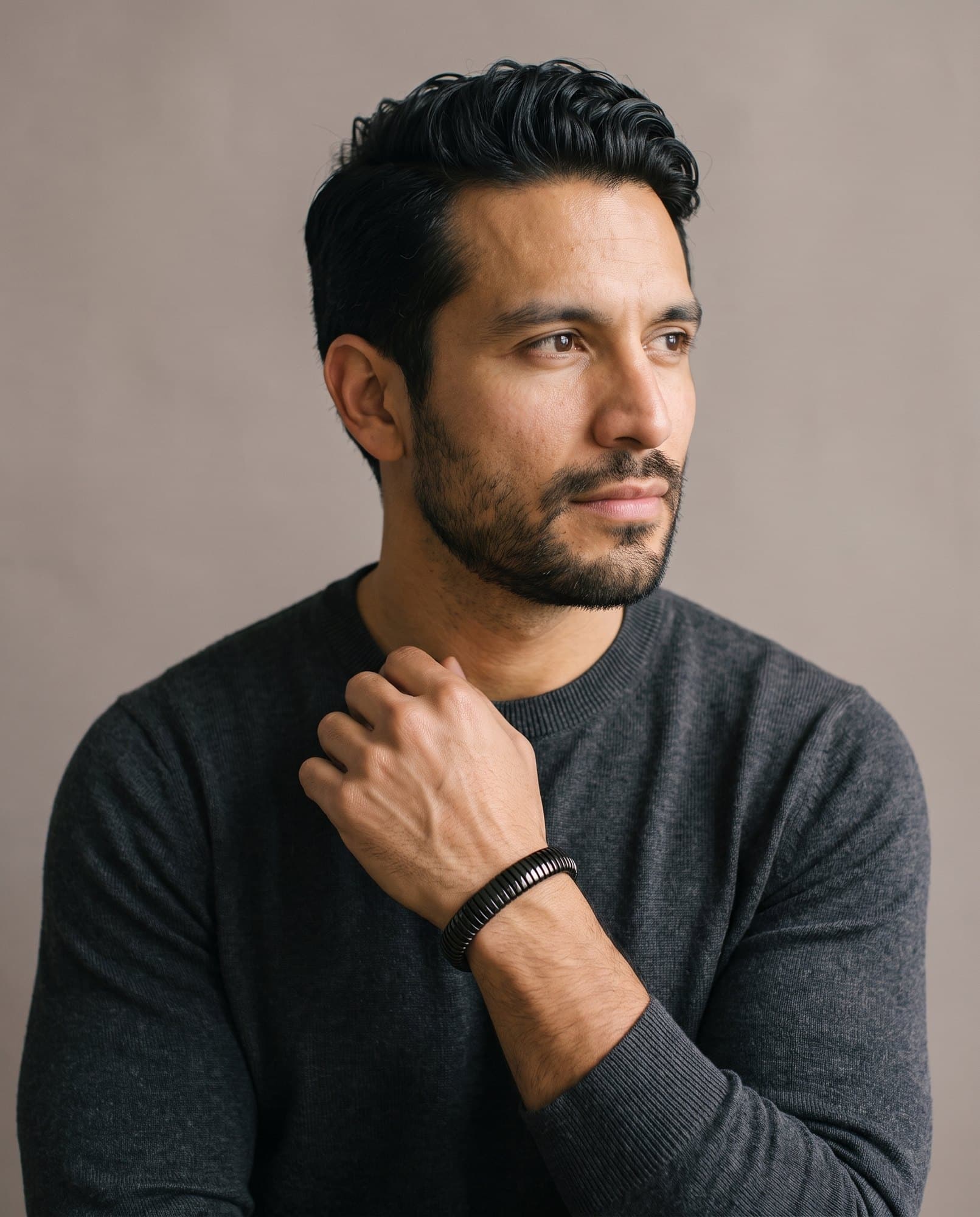 A man in a charcoal knit with his hand at his collarbone, the Coil Bangle Noir on his wrist.