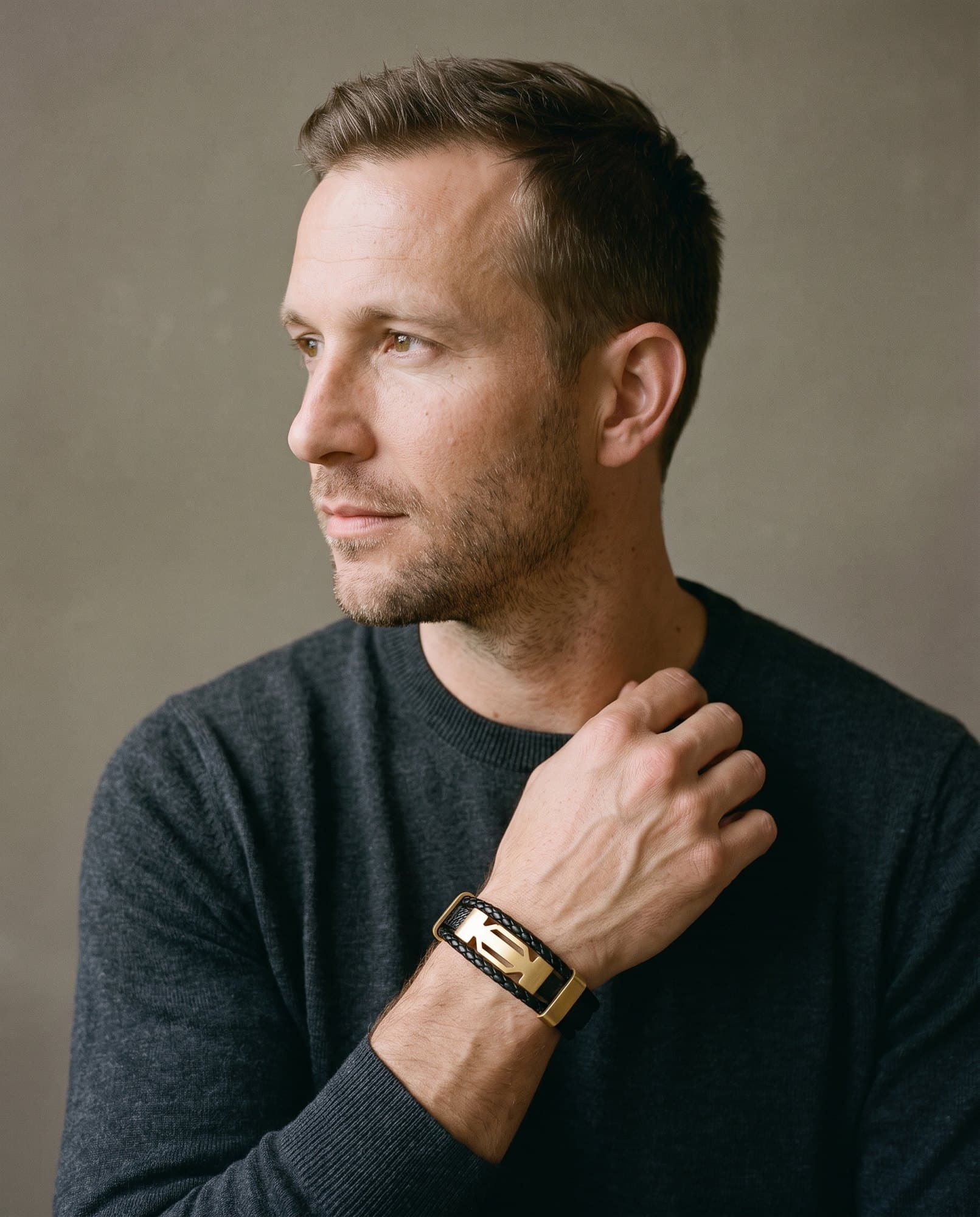 A man in a charcoal knit with his hand at his collarbone, the Deco Leather Cord on his wrist.