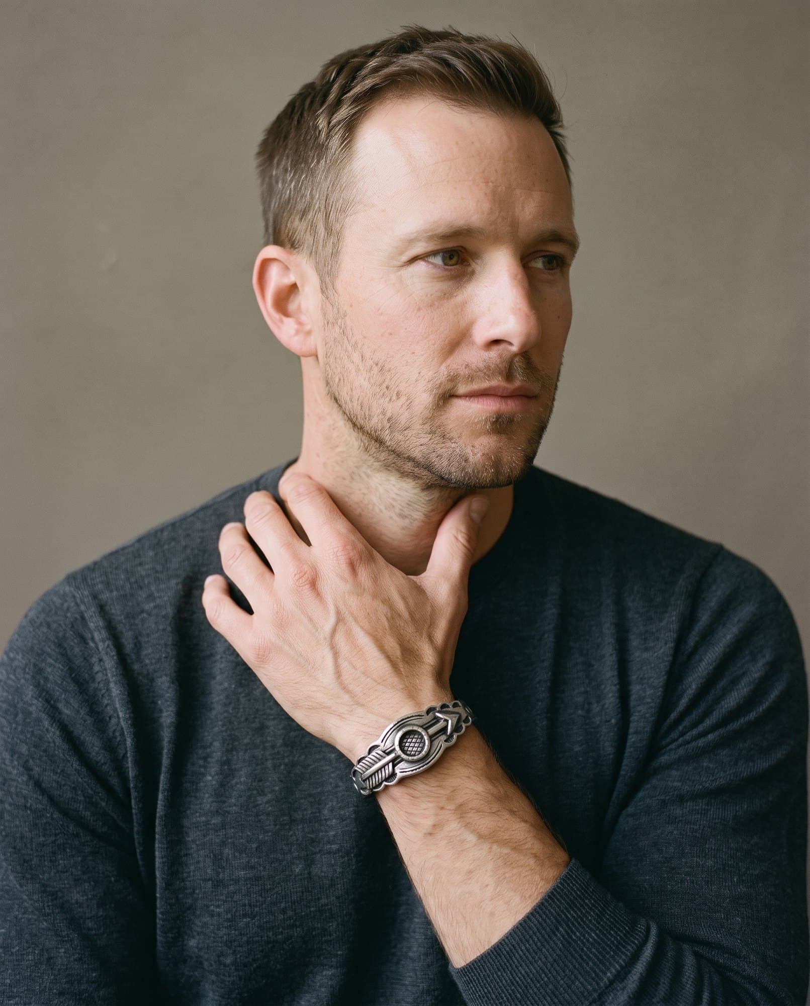 A man in a charcoal knit with his hand at his collarbone, the Delta Arrow Cuff on his wrist.