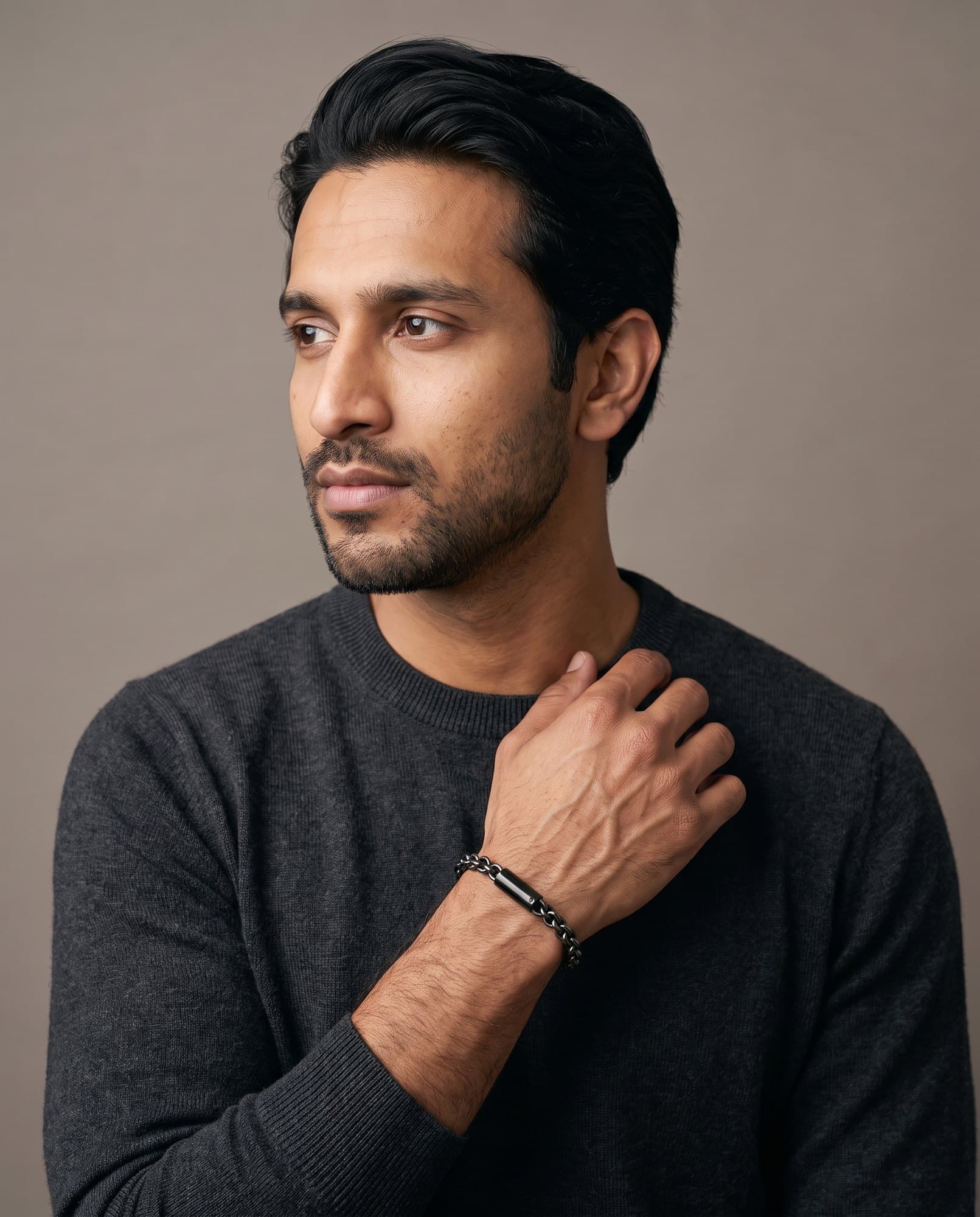 A man in a charcoal knit with his hand at his collarbone, the Delta Cable Chain on his wrist.