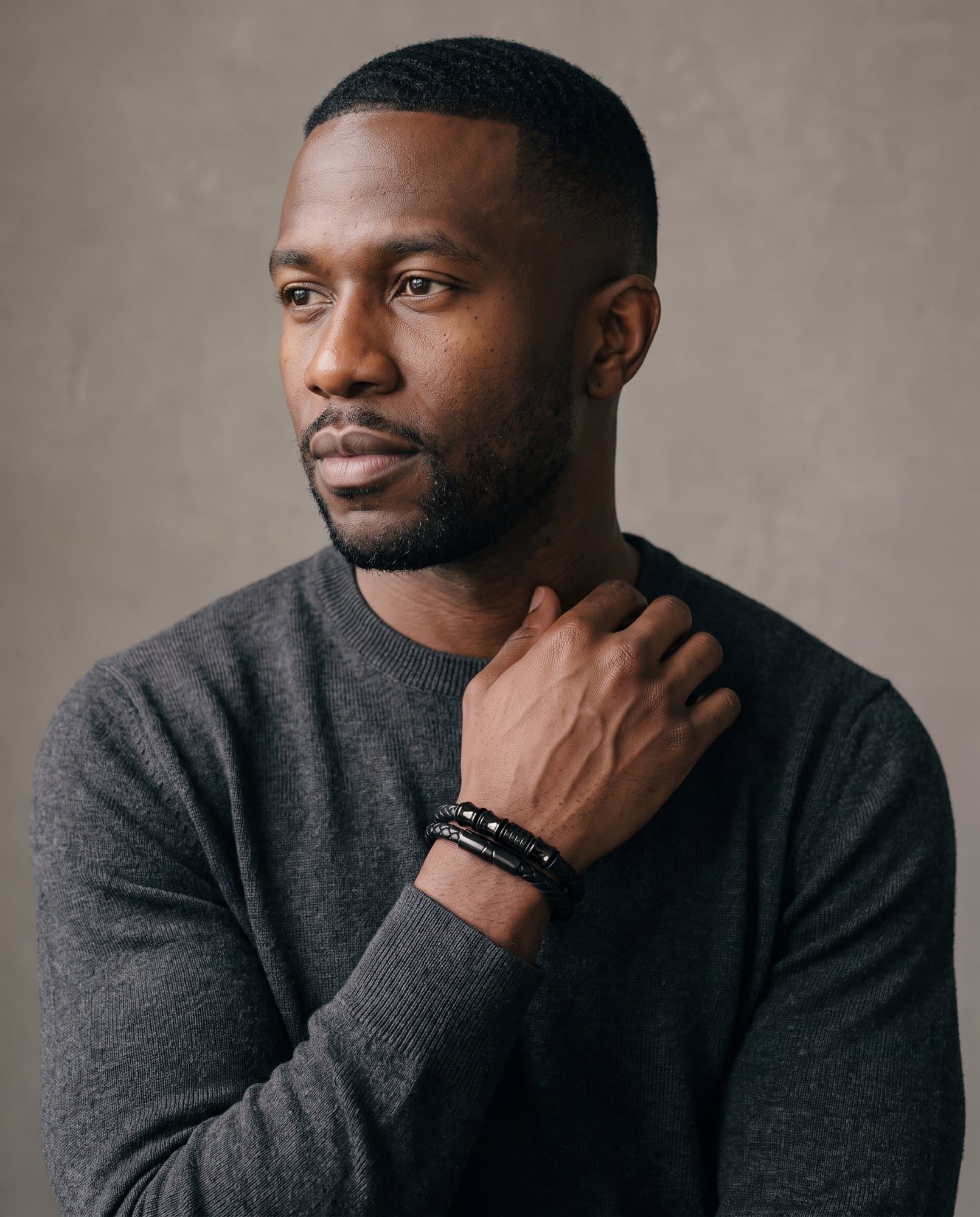 A man in a charcoal knit with his hand at his collarbone, the Double Braid Cord on his wrist.