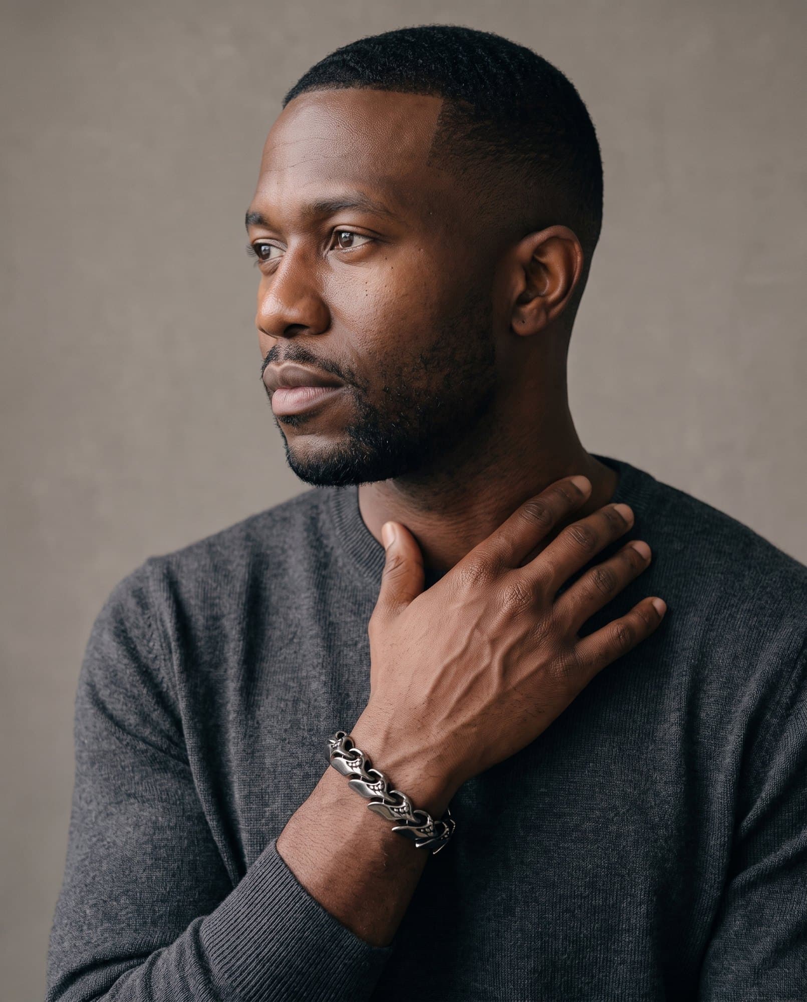 A man in a charcoal knit with his hand at his collarbone, the Flame Link Chain on his wrist.