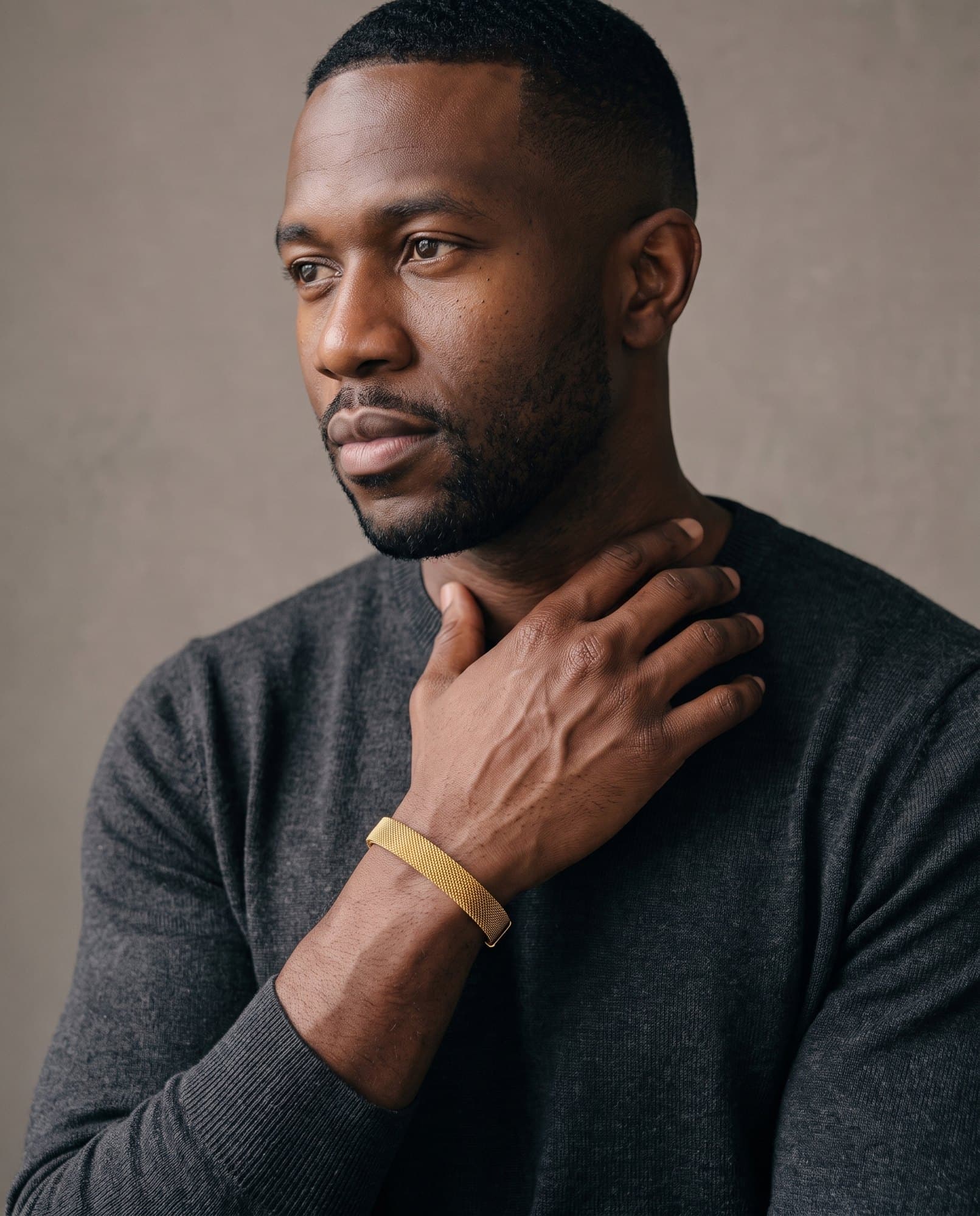 A man in a charcoal knit with his hand at his collarbone, the Giza Mesh Cuff on his wrist.