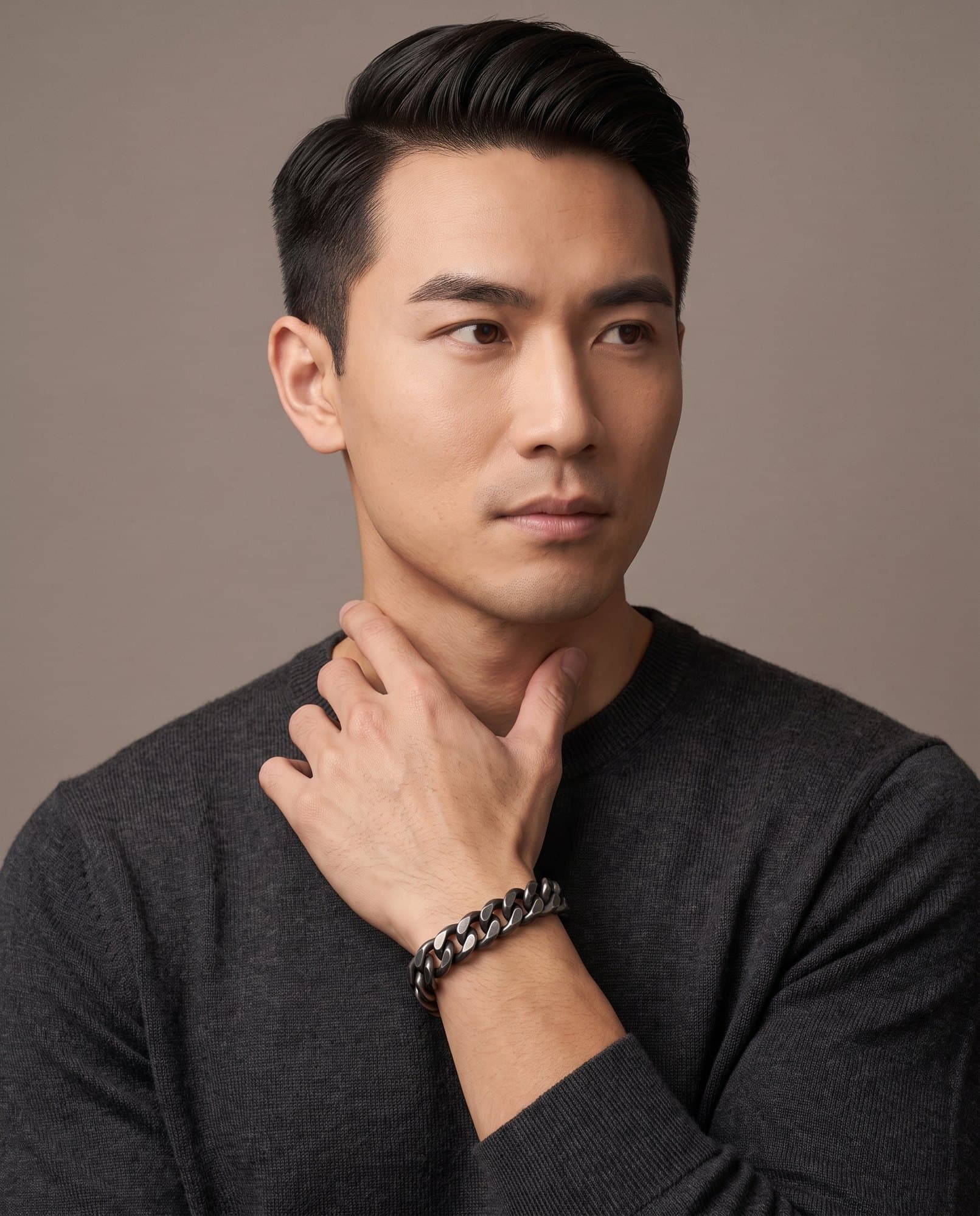 A man in a charcoal knit with his hand at his collarbone, the Gunmetal Curb Chain on his wrist.
