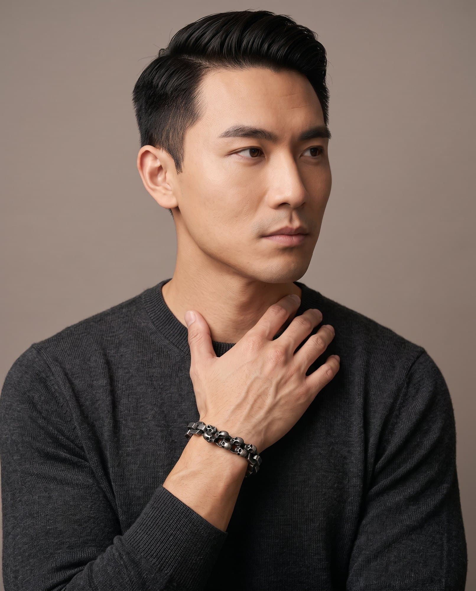 A man in a charcoal knit with his hand at his collarbone, the Hex Skull Chain on his wrist.