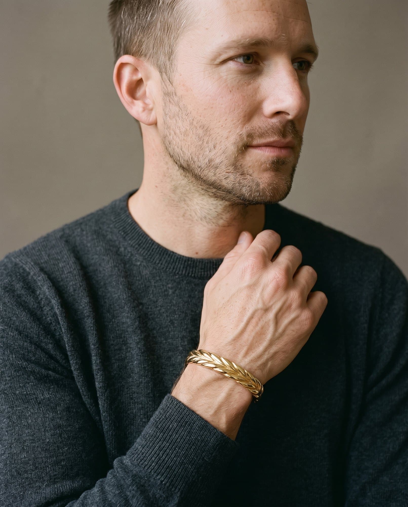 A man in a charcoal knit with his hand at his collarbone, the Karnak Braid Cuff on his wrist.