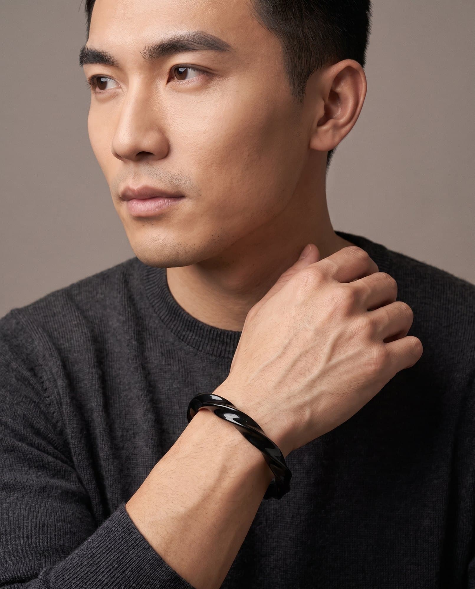 A man in a charcoal knit with his hand at his collarbone, the Karnak Noir Cuff on his wrist.