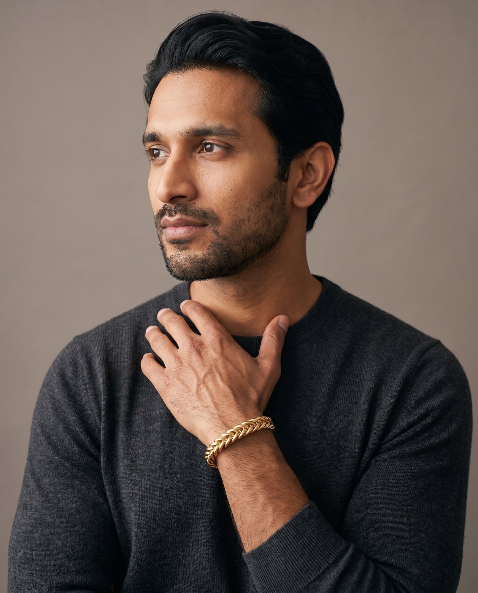 A man in a charcoal knit with his hand at his collarbone, the Karnak Plait Cuff on his wrist.