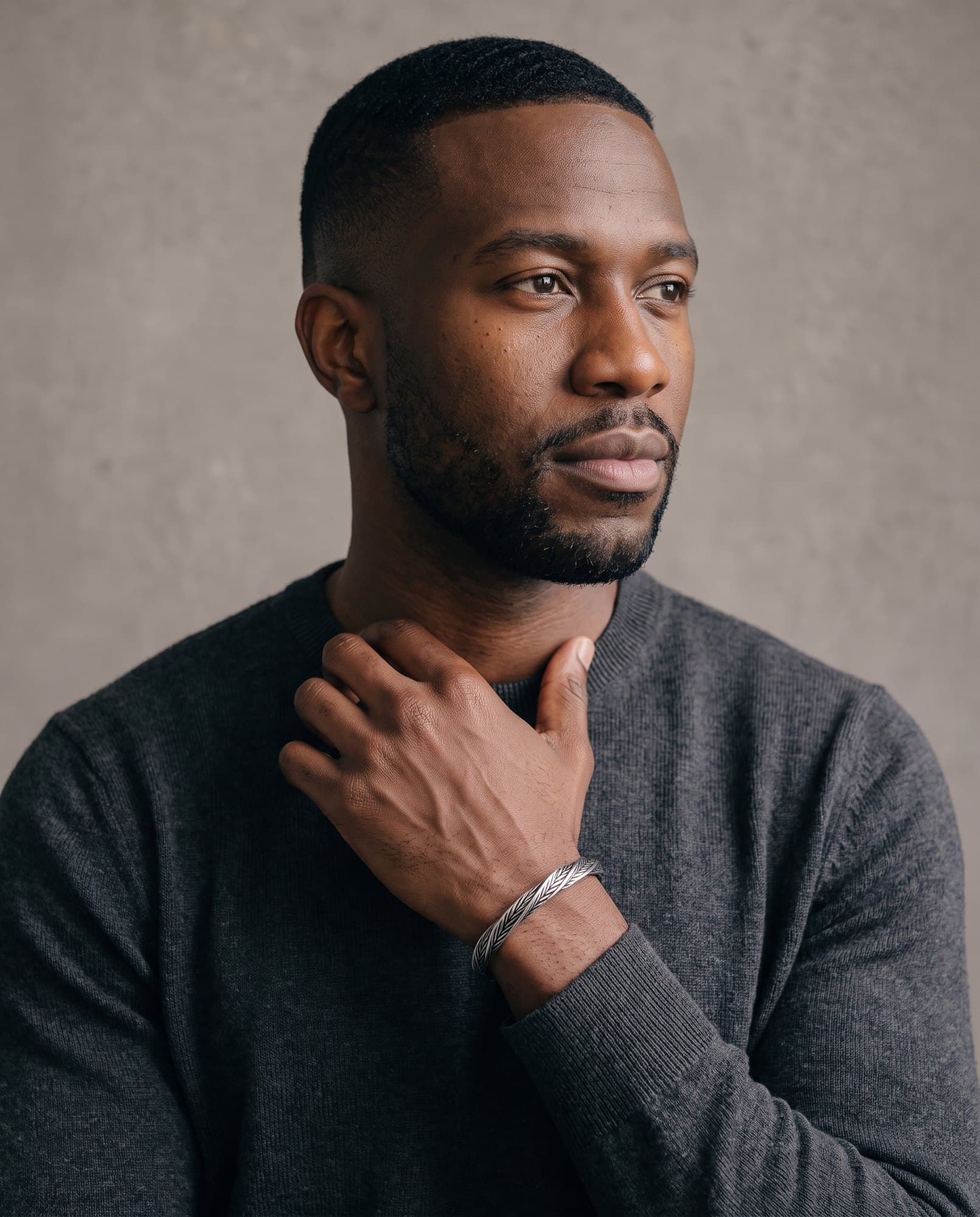A man in a charcoal knit with his hand at his collarbone, the Luxor Weave Cuff Antique on his wrist.