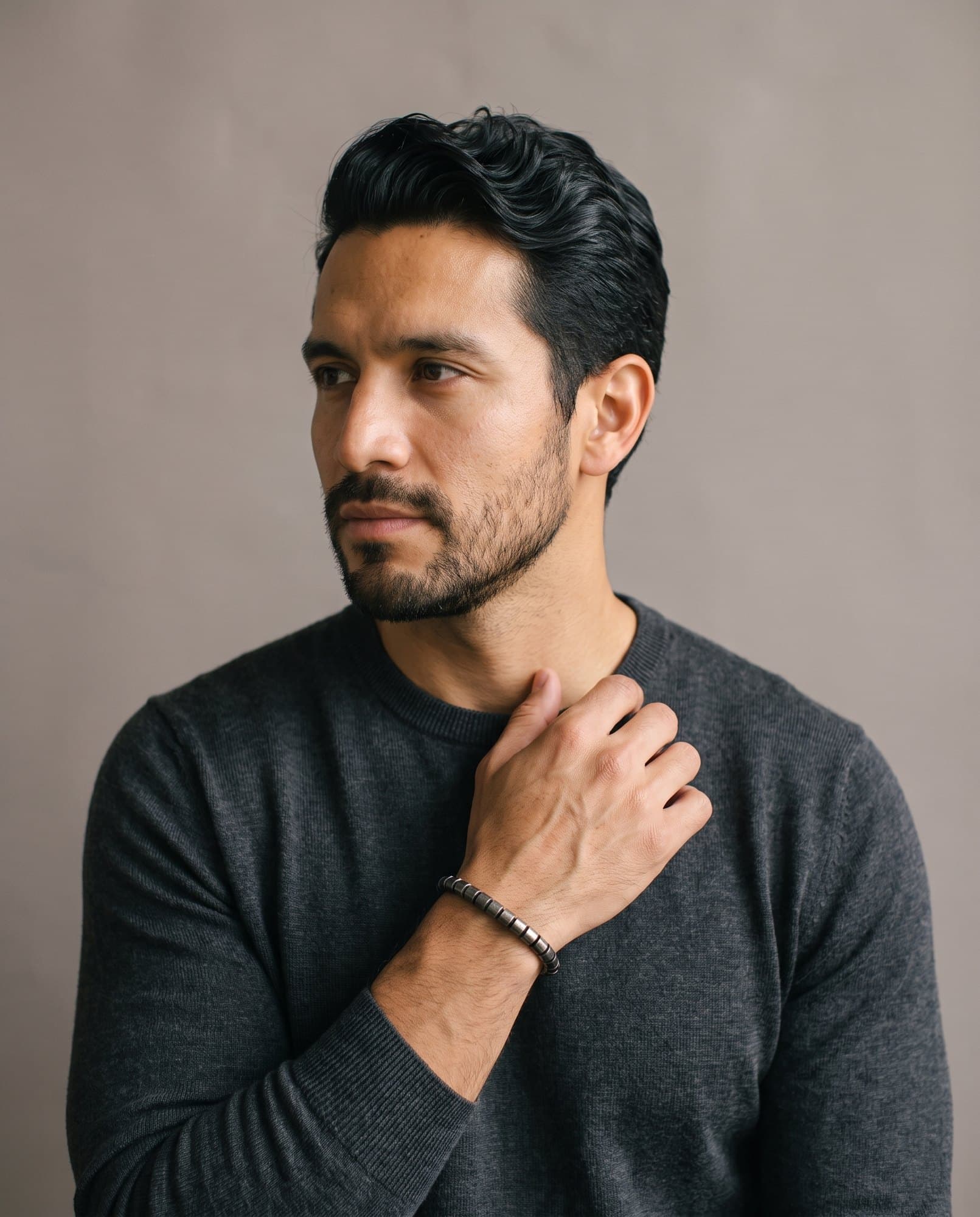 A man in a charcoal knit with his hand at his collarbone, the Meridian Barrel Chain on his wrist.