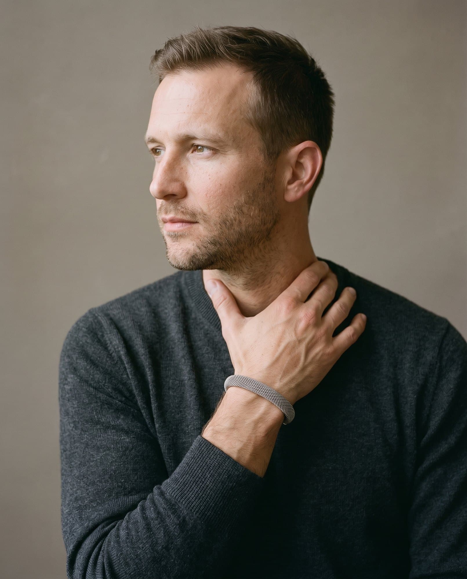 A man in a charcoal knit with his hand at his collarbone, the Meridian Mesh Cuff on his wrist.