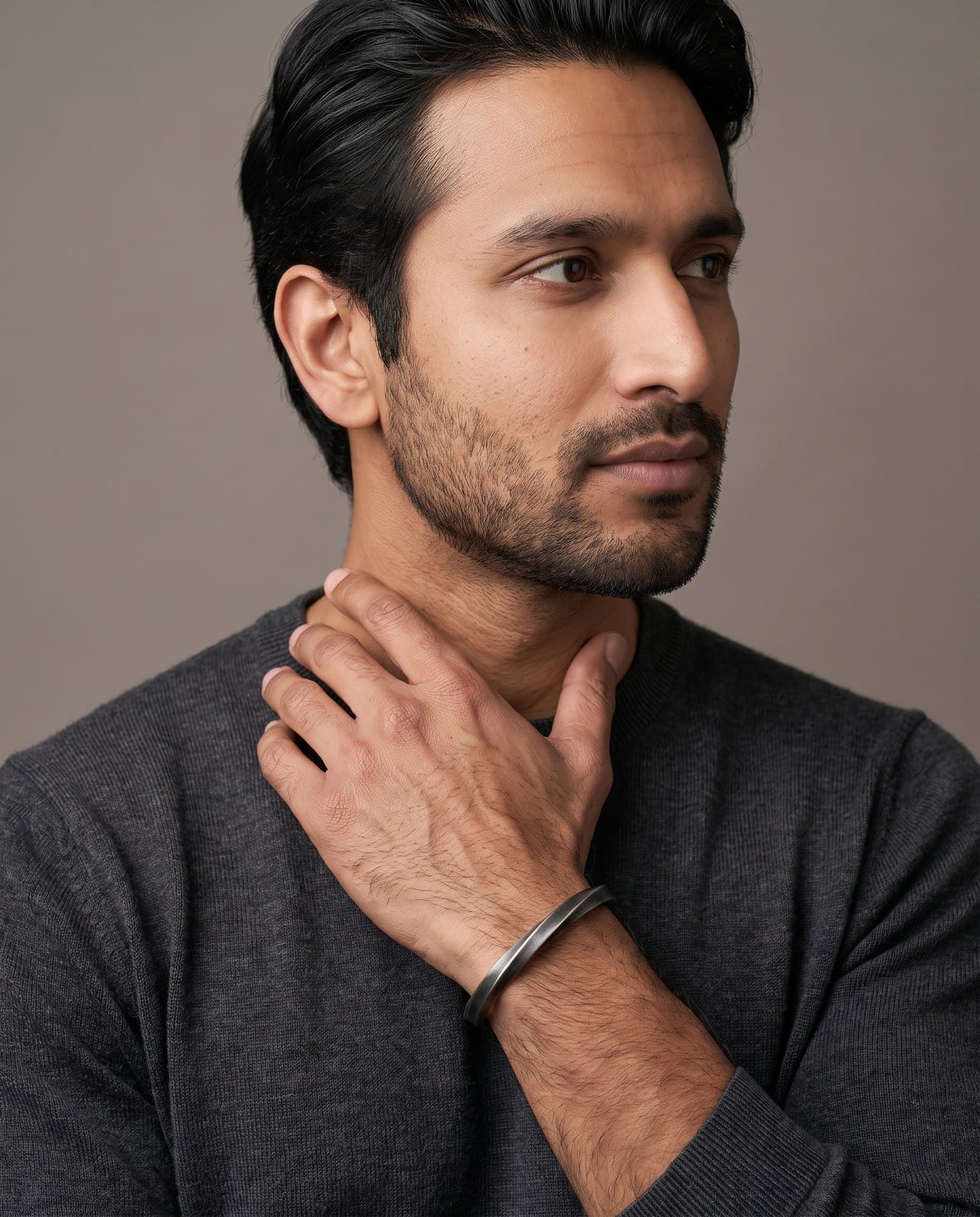 A man in a charcoal knit with his hand at his collarbone, the Meridian Twist Cuff on his wrist.