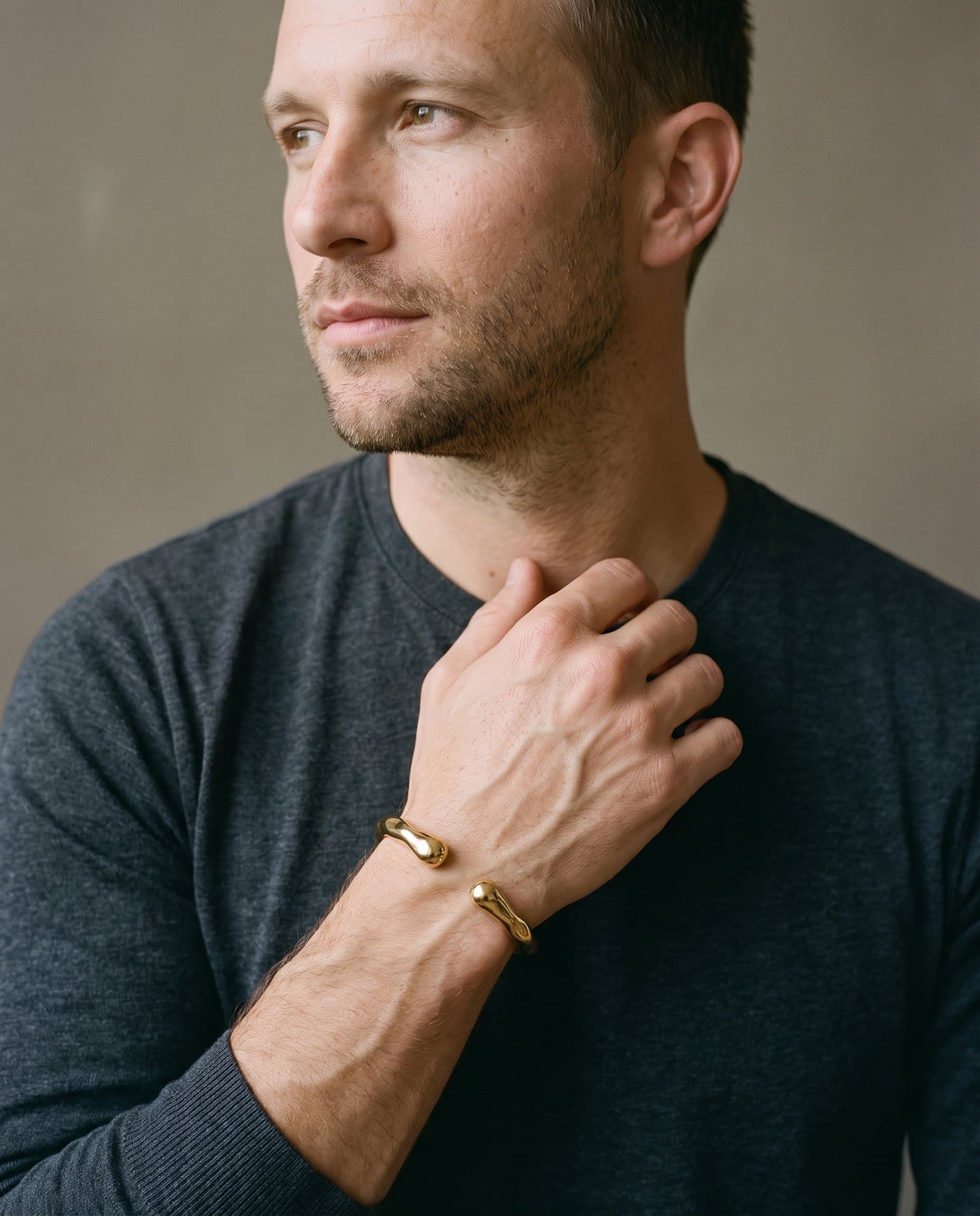 A man in a charcoal knit with his hand at his collarbone, the Molten Droplet Cuff on his wrist.