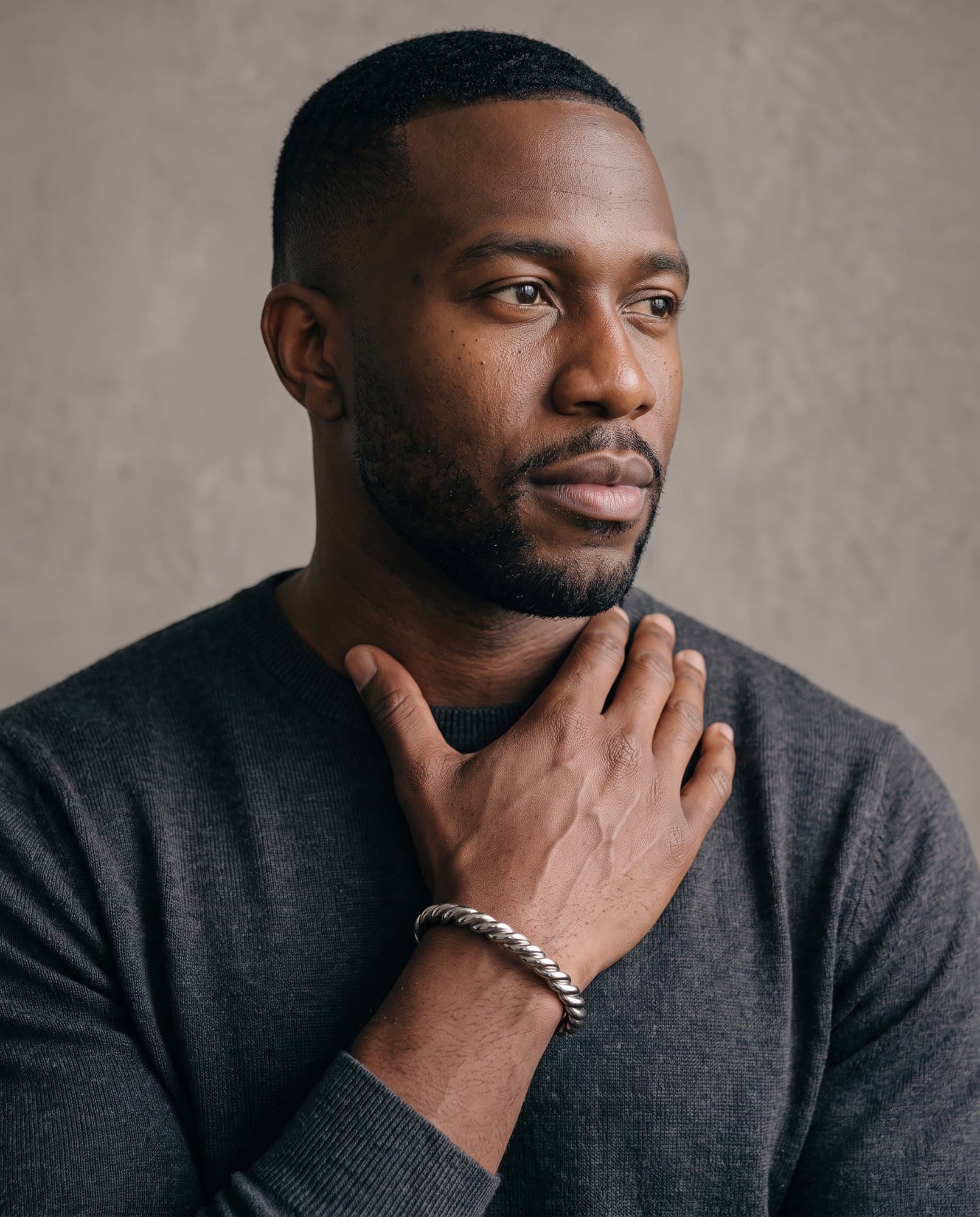A man in a charcoal knit with his hand at his collarbone, the Nile Rope Cuff on his wrist.