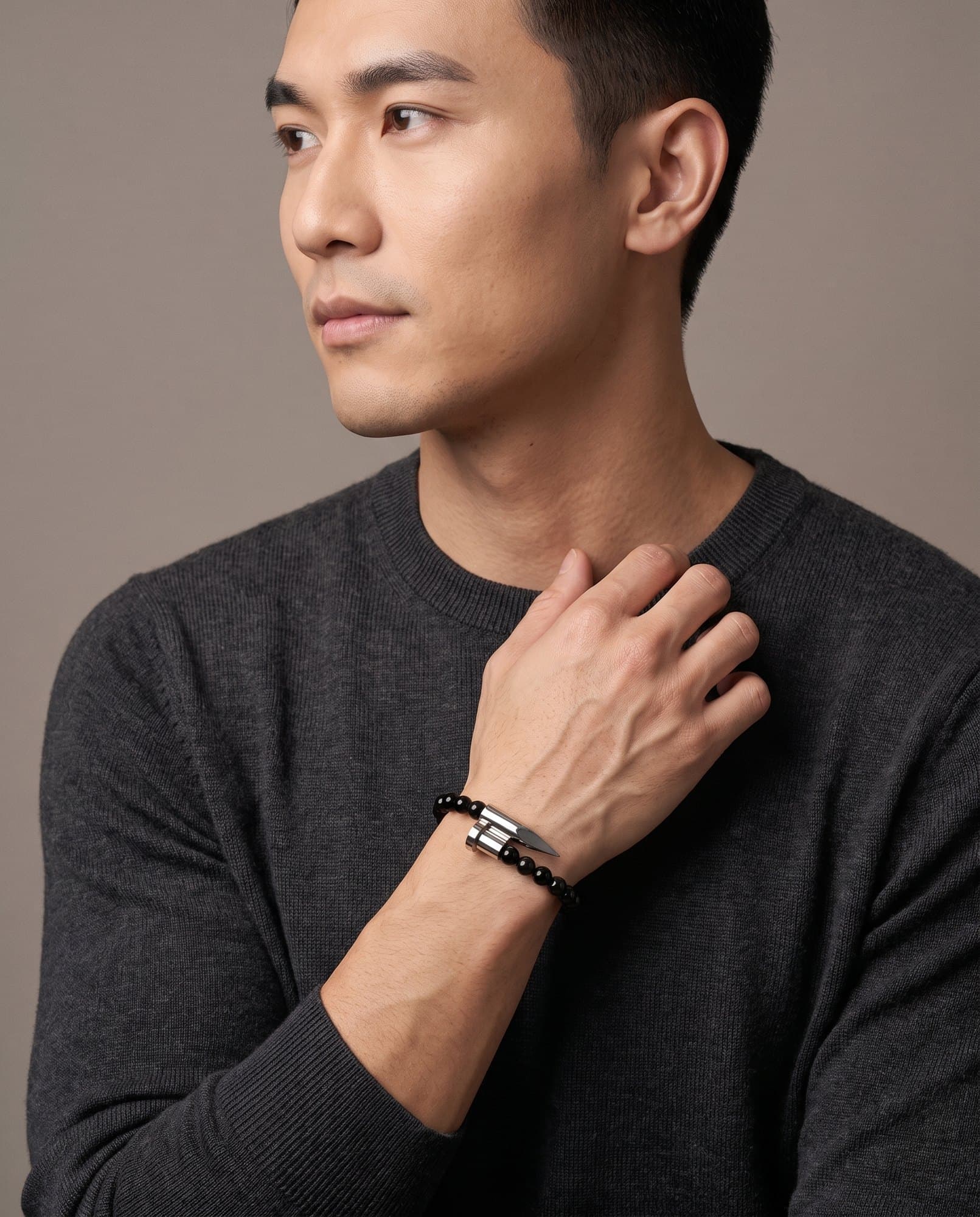 A man in a charcoal knit with his hand at his collarbone, the Onyx Spike Bracelet on his wrist.
