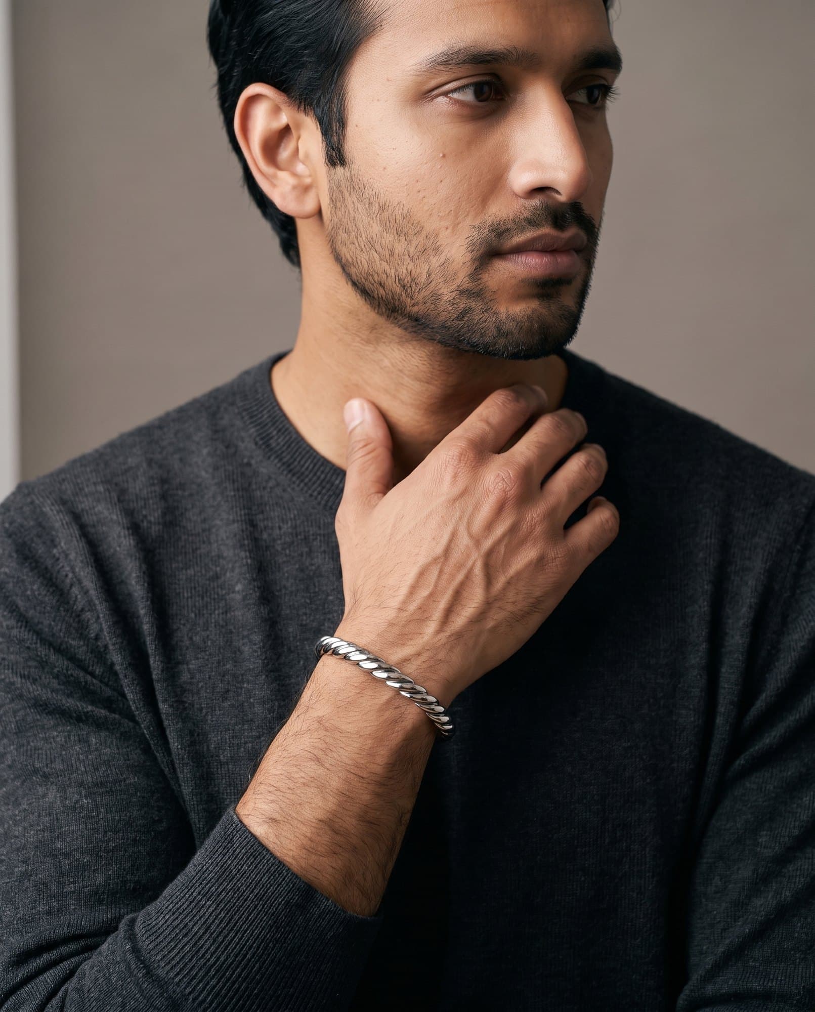 A man in a charcoal knit with his hand at his collarbone, the Pharaoh Wheat Cuff on his wrist.