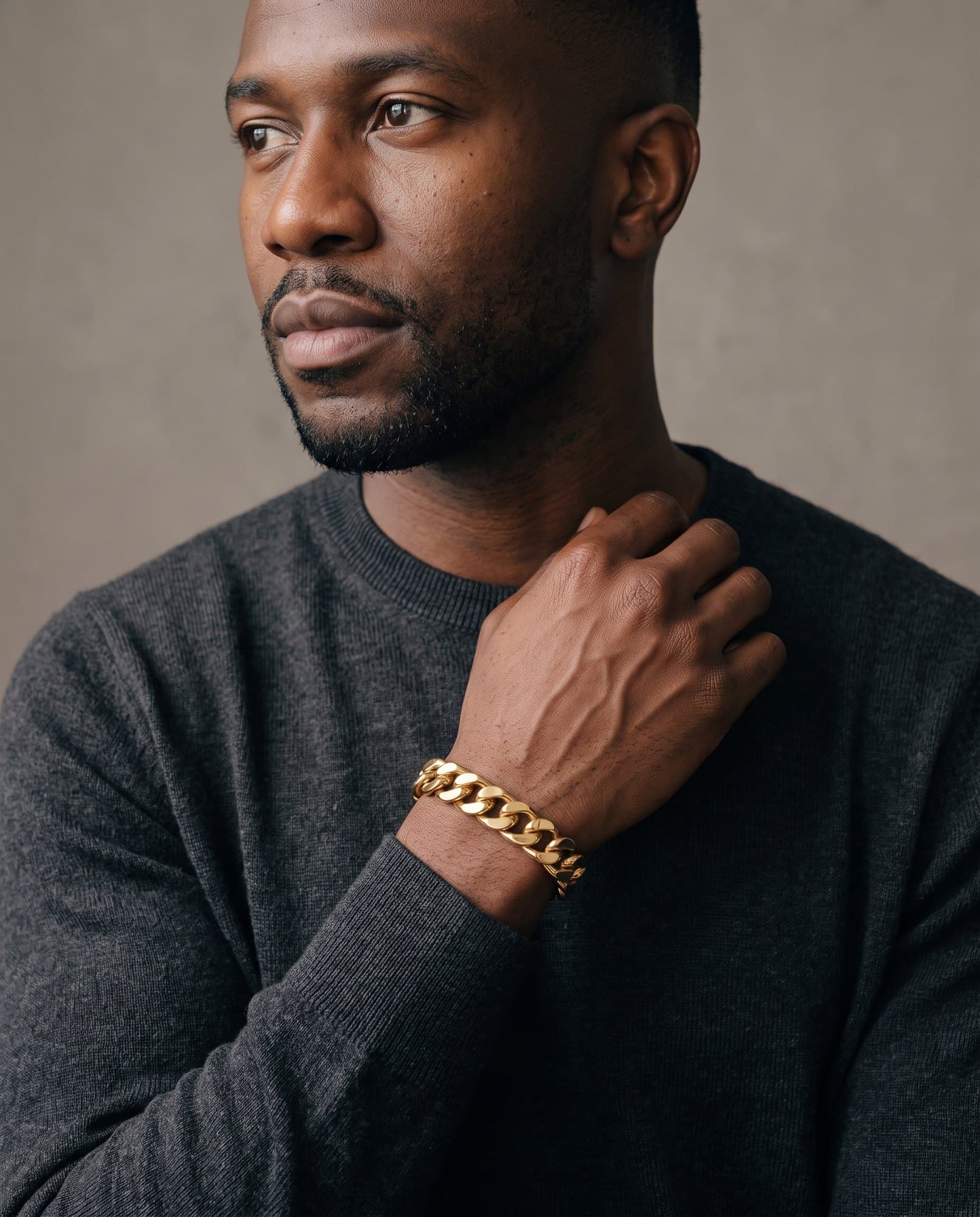 A man in a charcoal knit with his hand at his collarbone, the Pillar Link Cuff Gold on his wrist.
