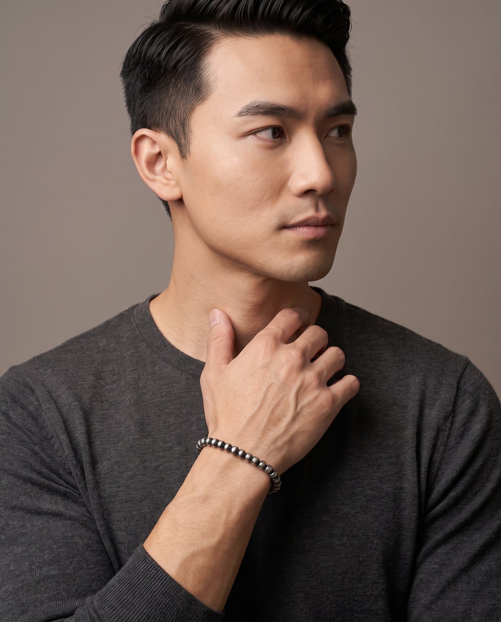 A man in a charcoal knit with his hand at his collarbone, the Rondel Bead Chain on his wrist.