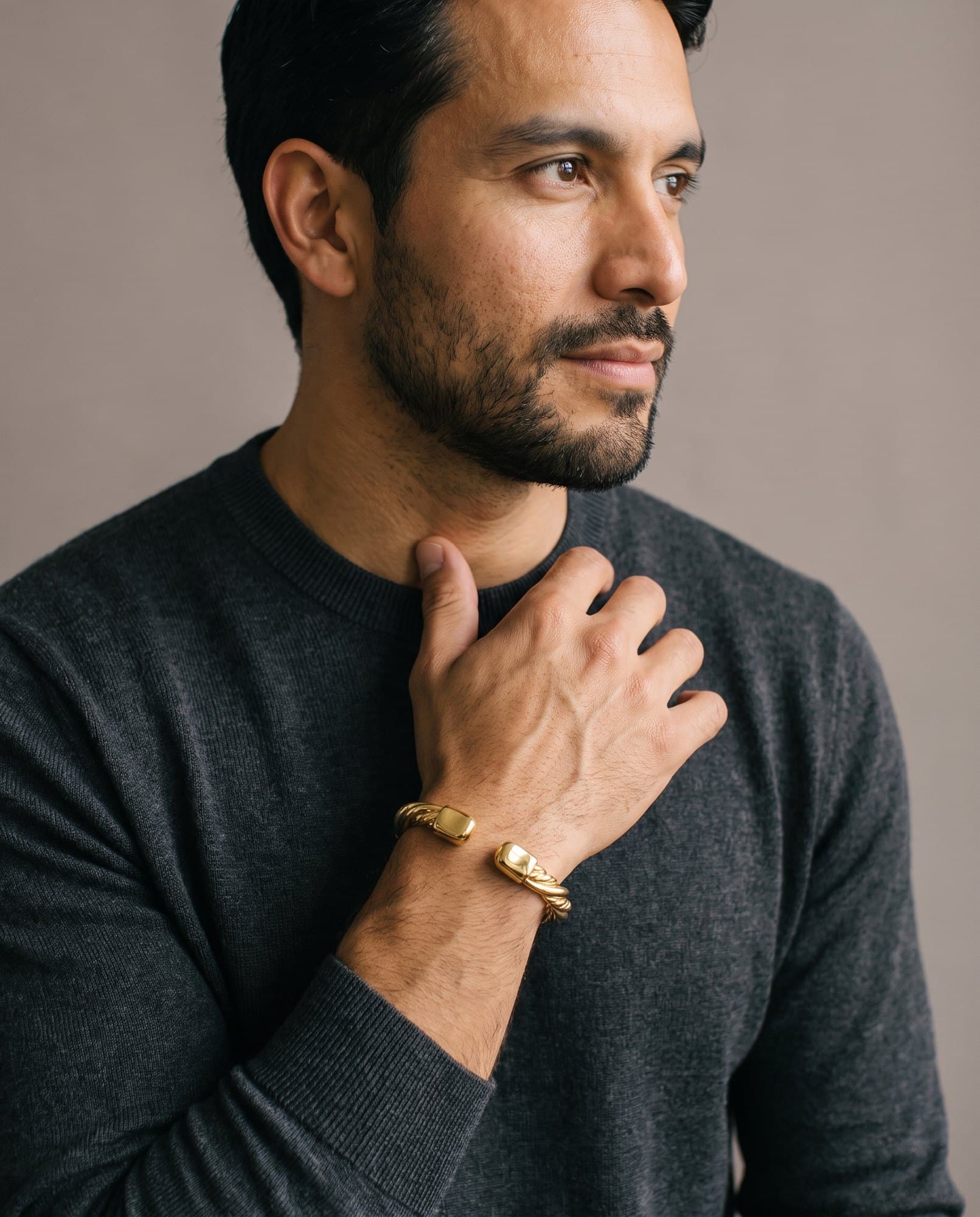 A man in a charcoal knit with his hand at his collarbone, the Scarab Twist Cuff on his wrist.