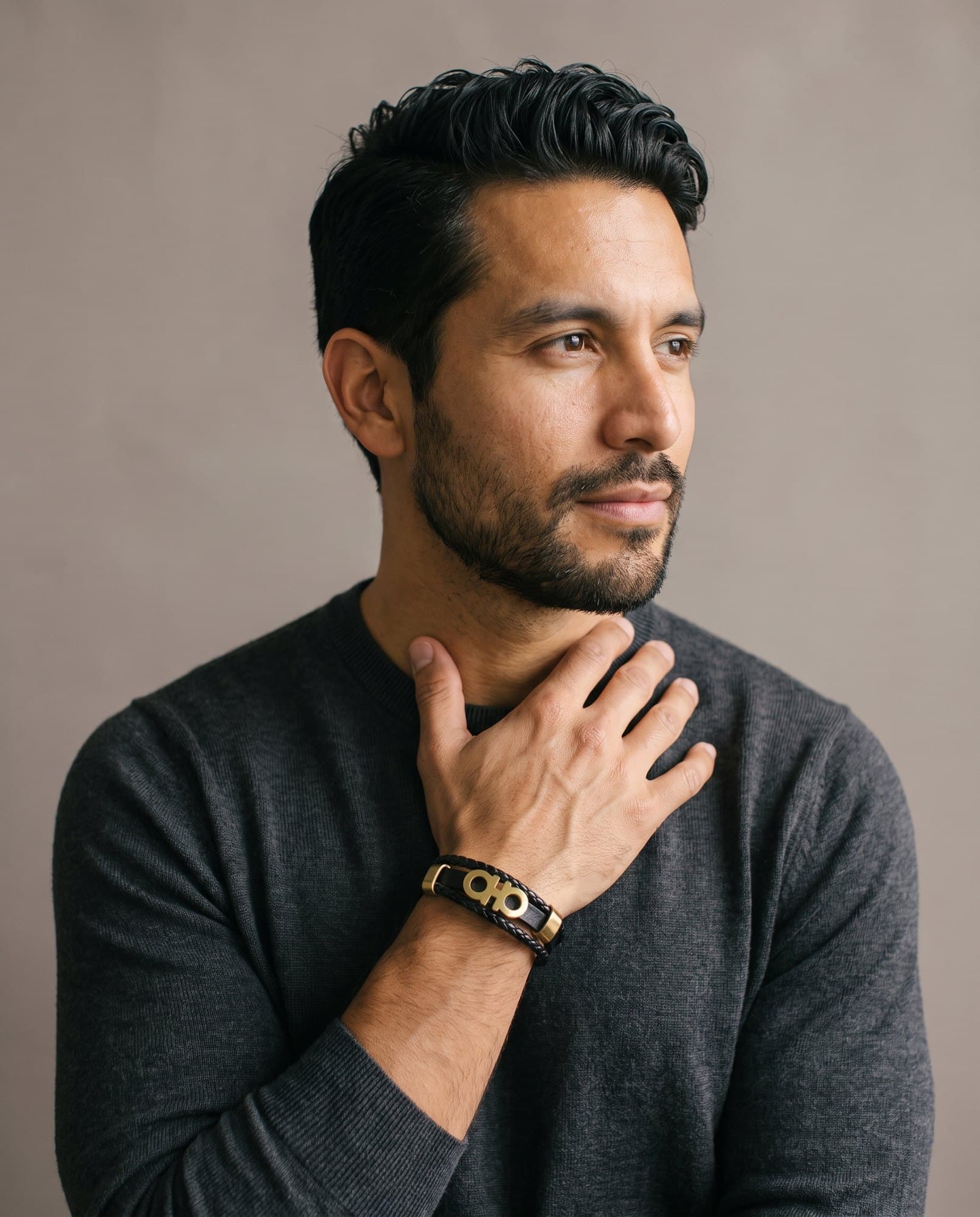 A man in a charcoal knit with his hand at his collarbone, the Sovereign Loop Wrap on his wrist.