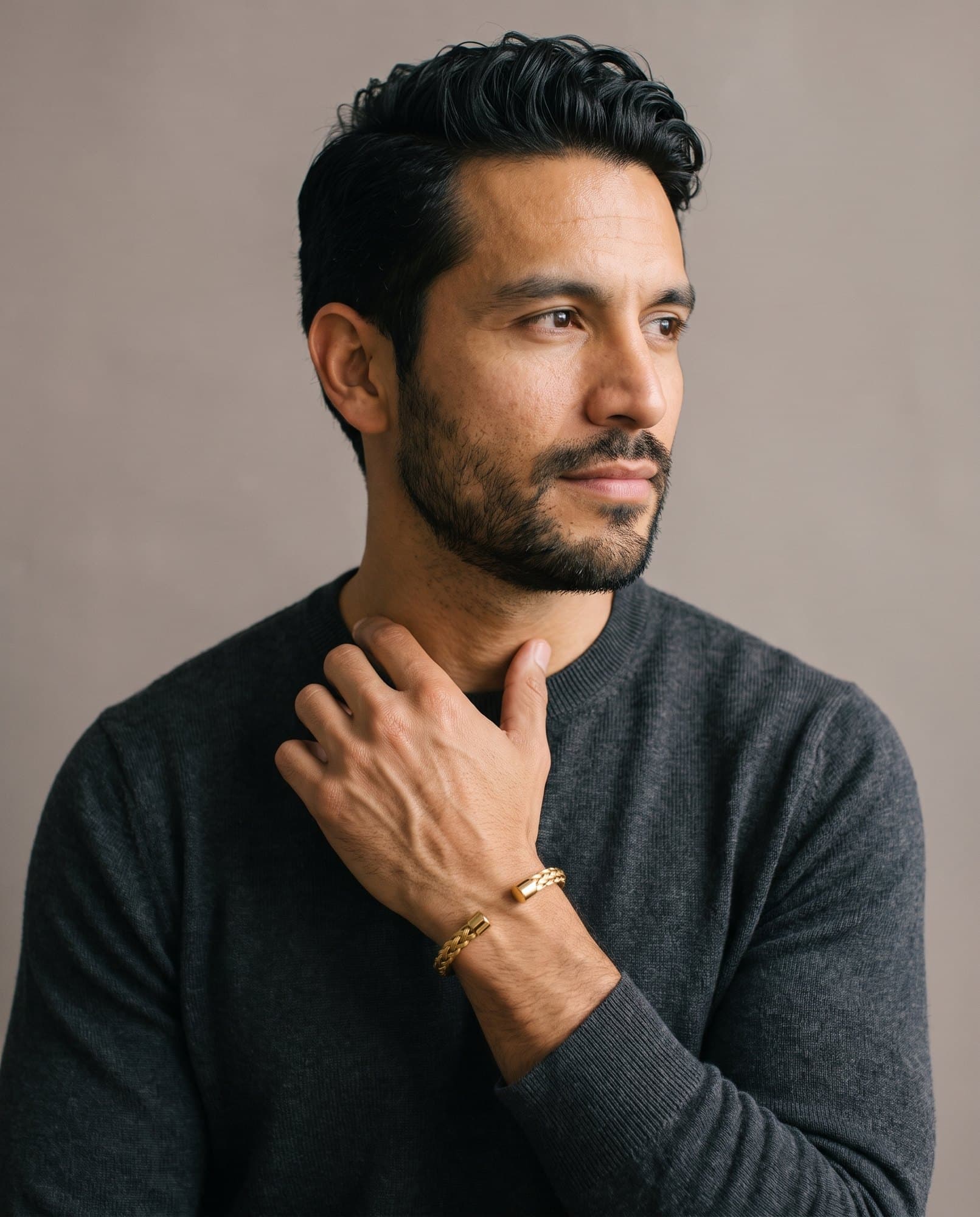 A man in a charcoal knit with his hand at his collarbone, the Sovereign Plait Cuff on his wrist.