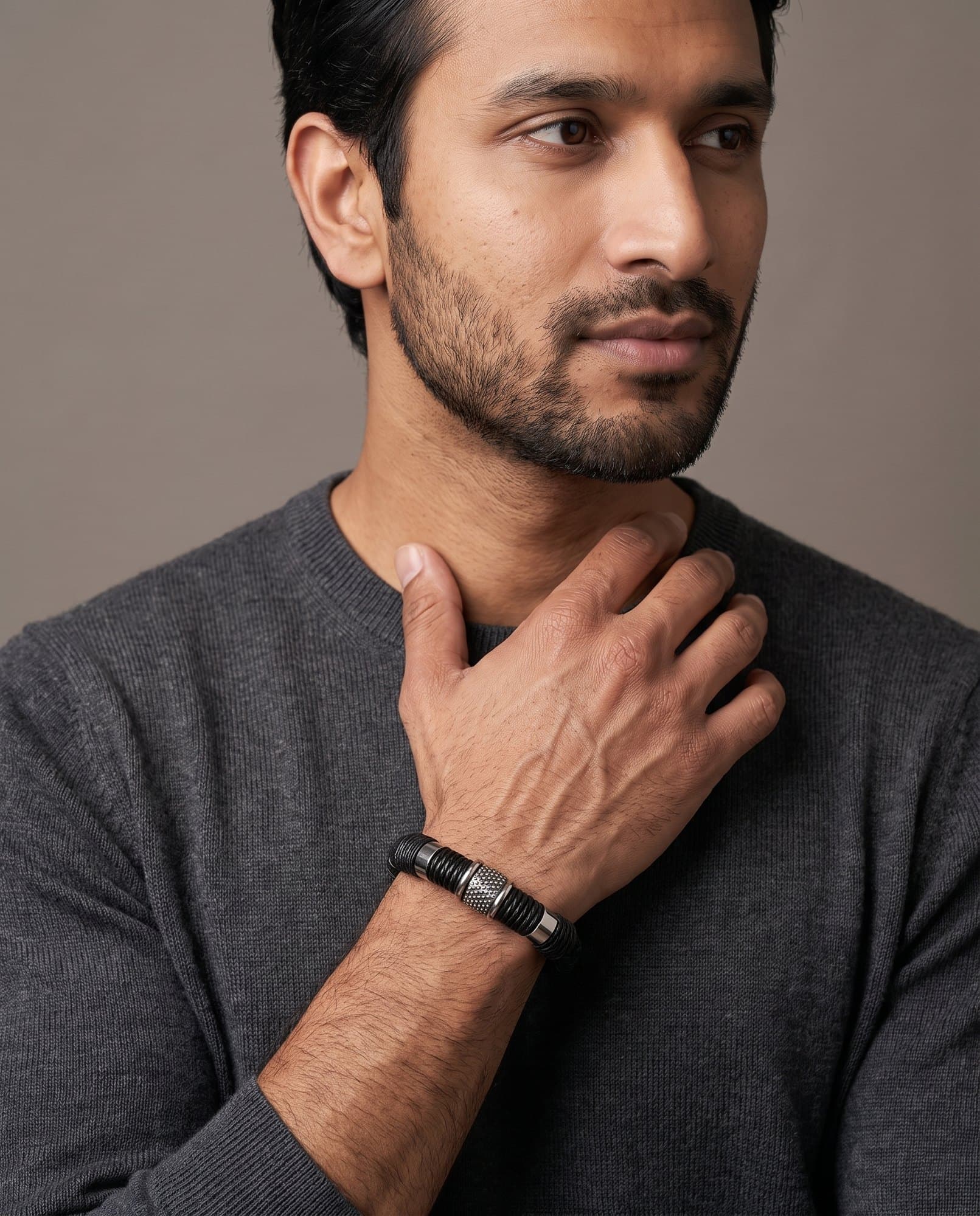 A man in a charcoal knit with his hand at his collarbone, the Stud Leather Cord on his wrist.