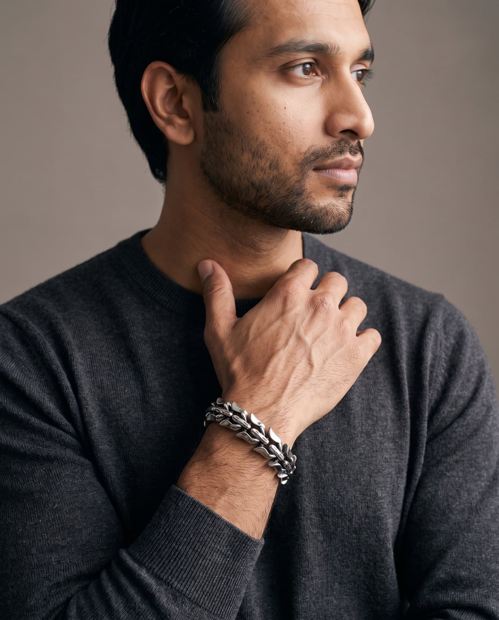 A man in a charcoal knit with his hand at his collarbone, the Talon Link Chain on his wrist.