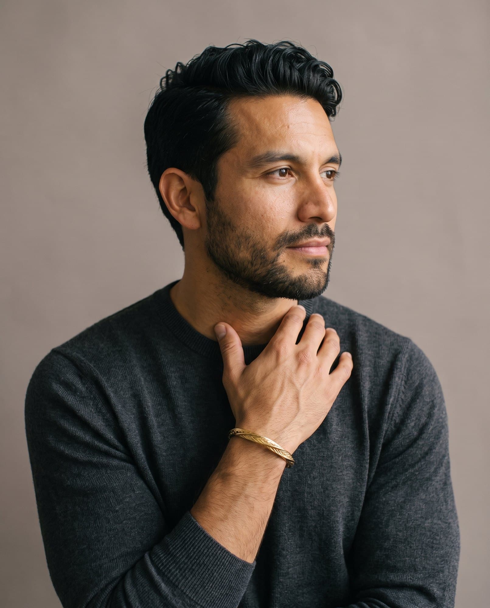A man in a charcoal knit with his hand at his collarbone, the Thebes Chevron Cuff on his wrist.