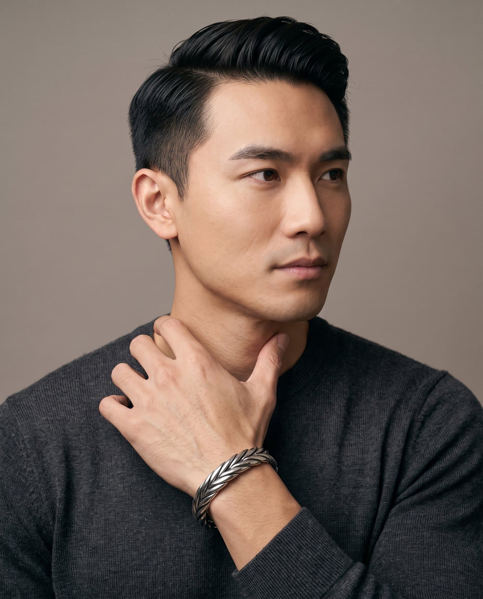 A man in a charcoal knit with his hand at his collarbone, the Thebes Weave Cuff on his wrist.