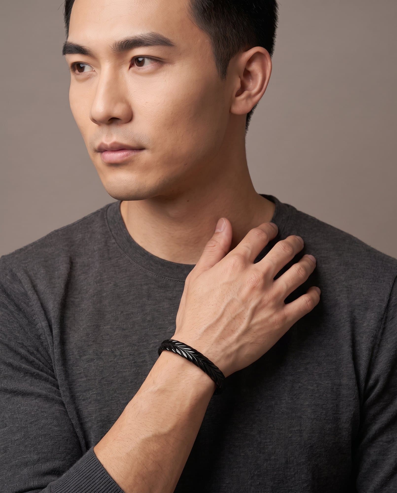 A man in a charcoal knit with his hand at his collarbone, the Thebes Weave Cuff Noir on his wrist.