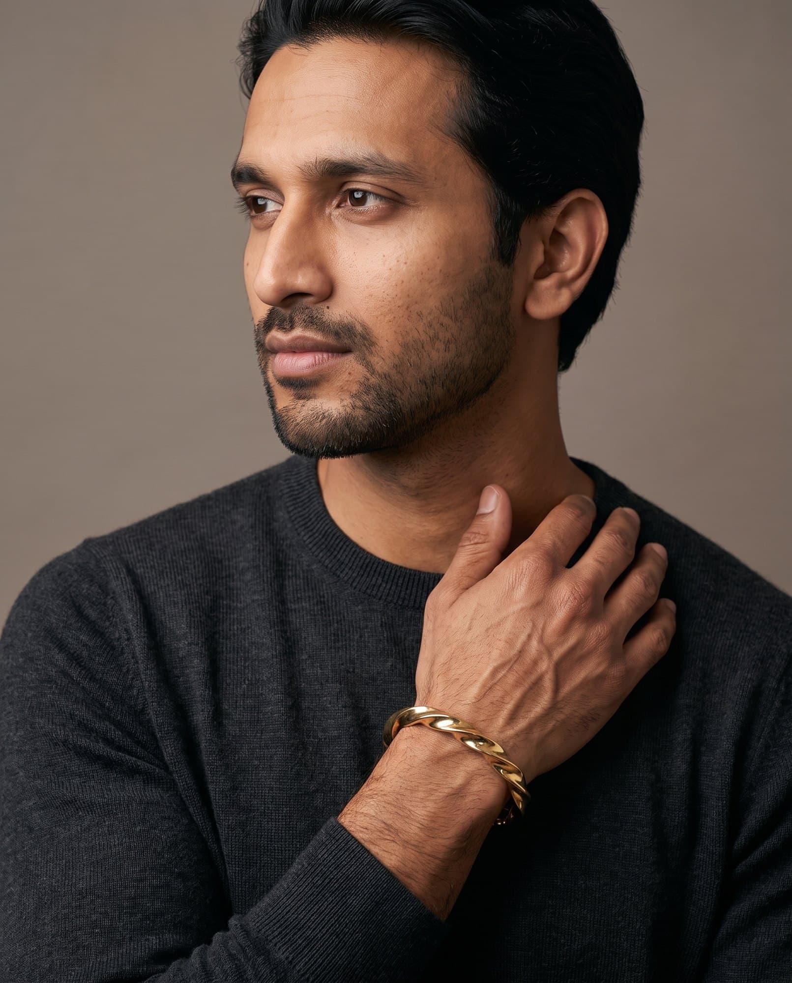 A man in a charcoal knit with his hand at his collarbone, the Vizier Wedge Cuff on his wrist.