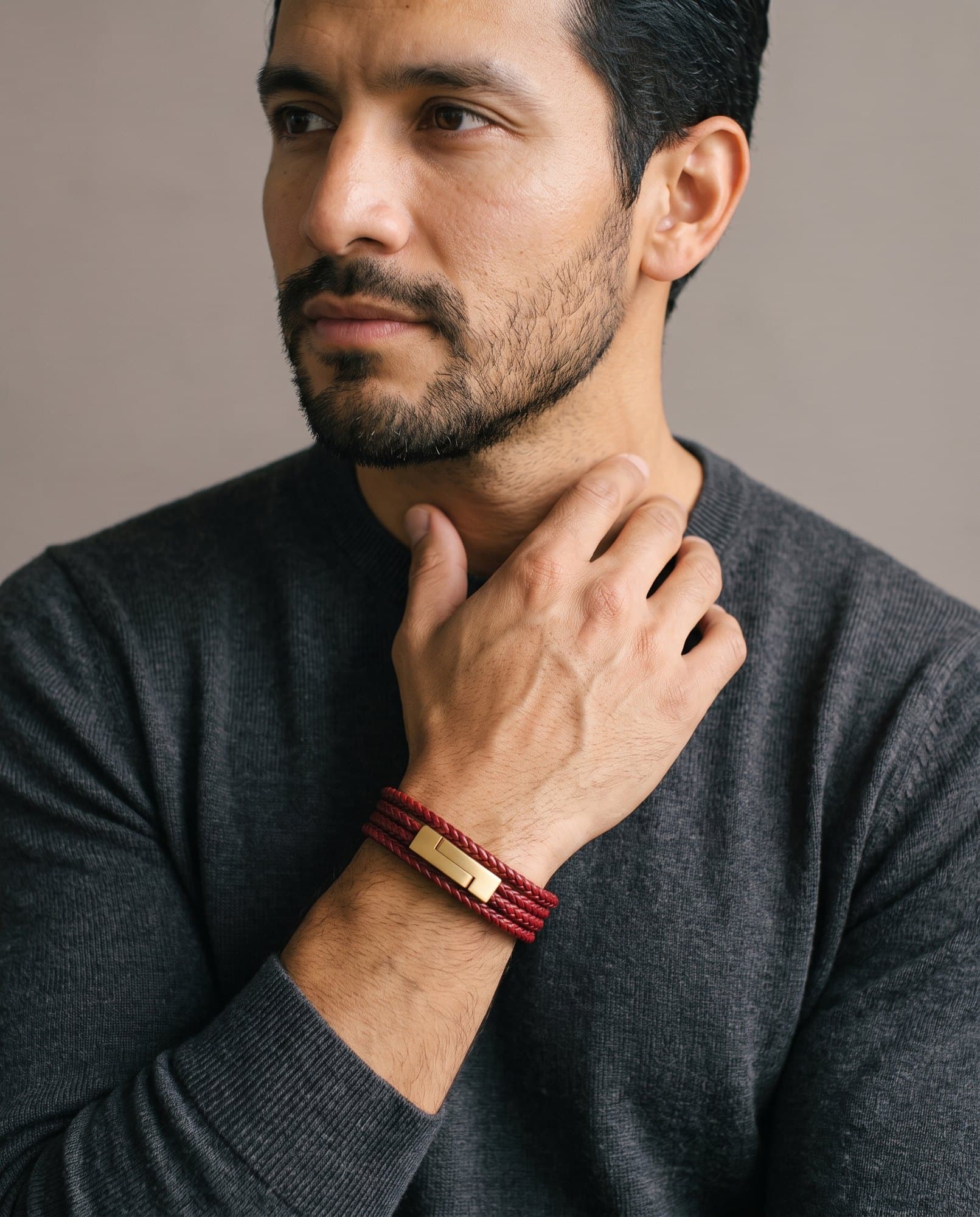 A man in a charcoal knit with his hand at his collarbone, the Voyage Wrap on his wrist.