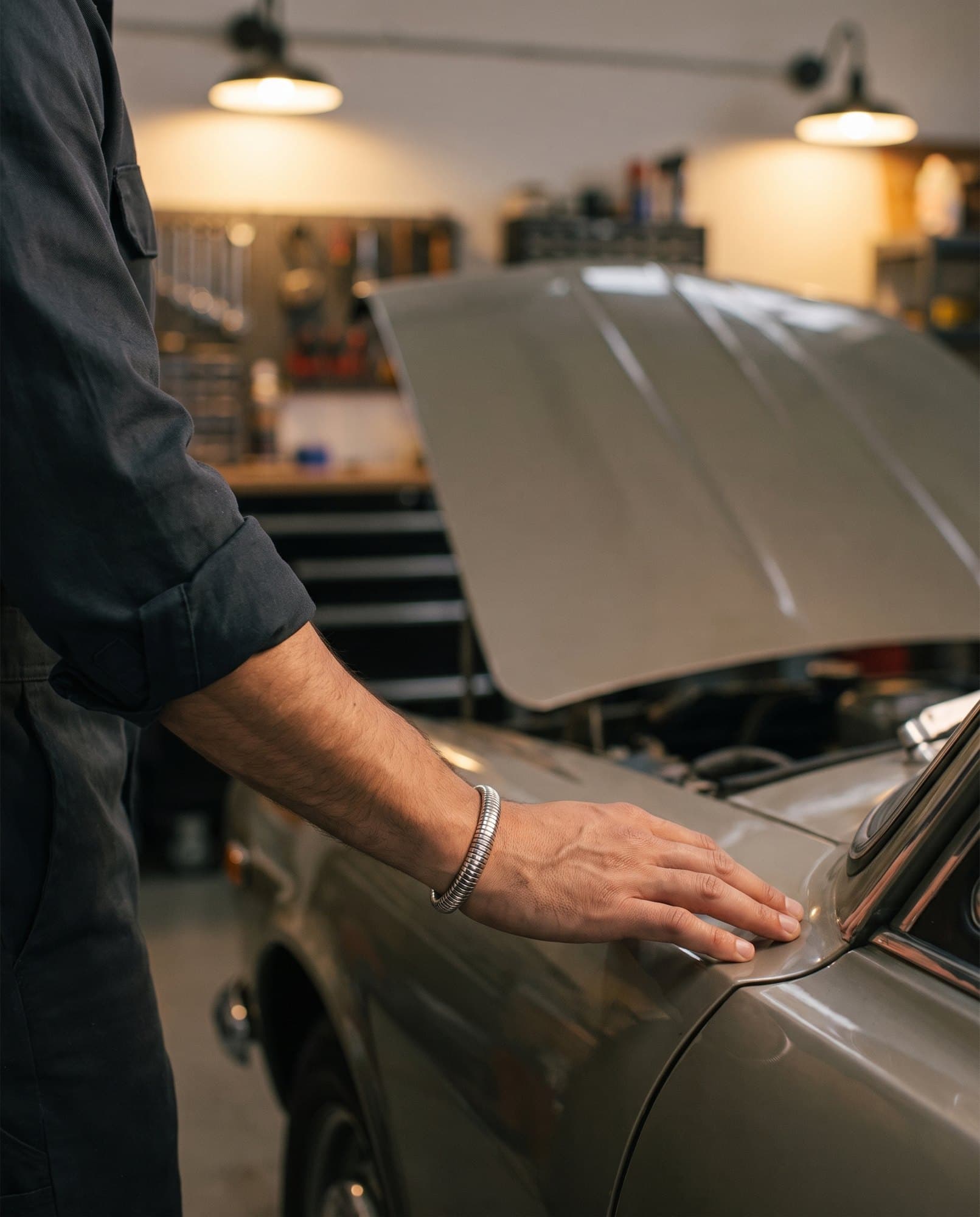 A strong hand resting flat on a car fender, a ribbed steel bangle at the wrist.