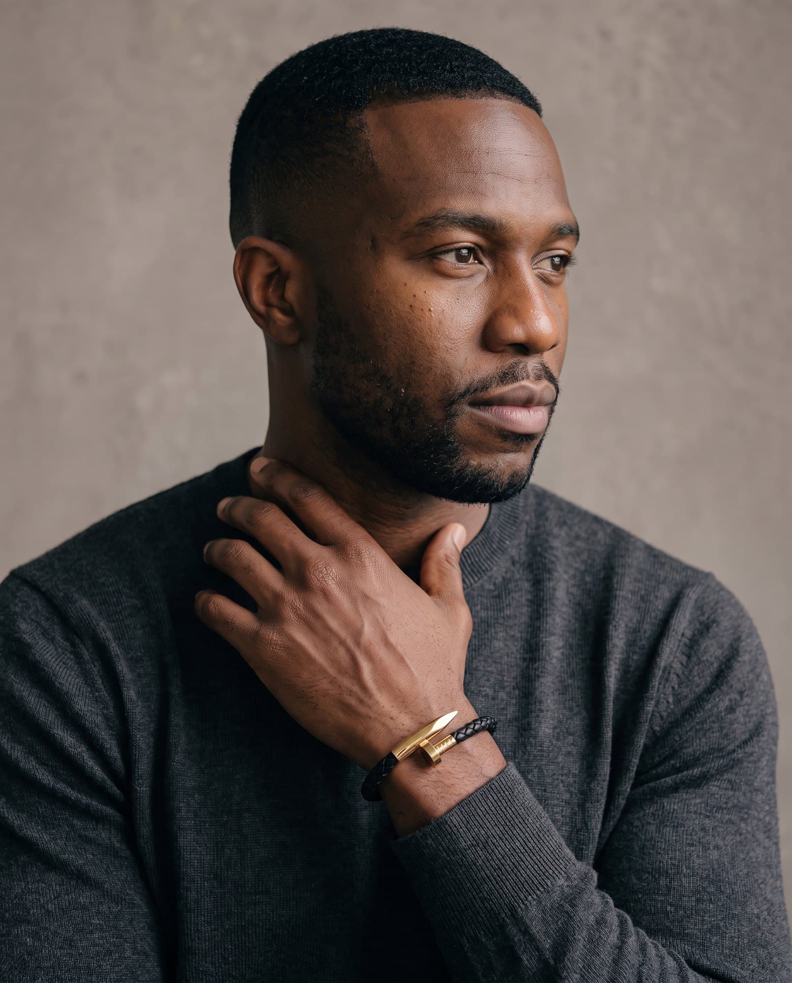 A man in a charcoal knit with his hand at his collarbone, the Nail Point Cuff on his wrist.