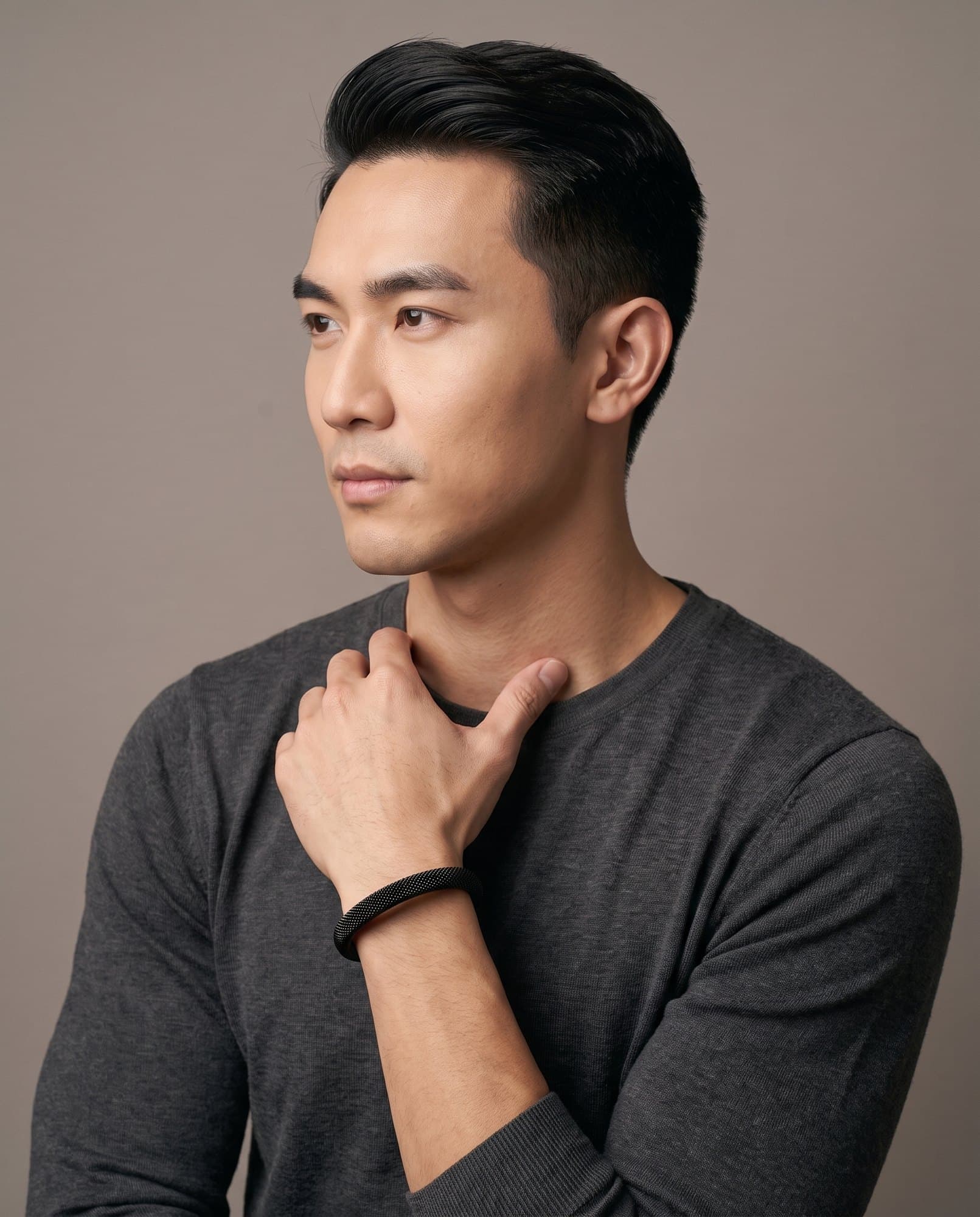 A man in a charcoal knit with his hand at his collarbone, the Noir Mesh Cuff on his wrist.