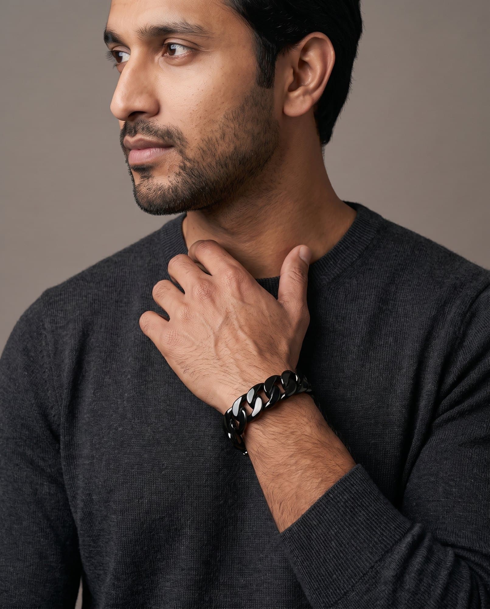 A man in a charcoal knit with his hand at his collarbone, the Obelisk Curb Cuff on his wrist.