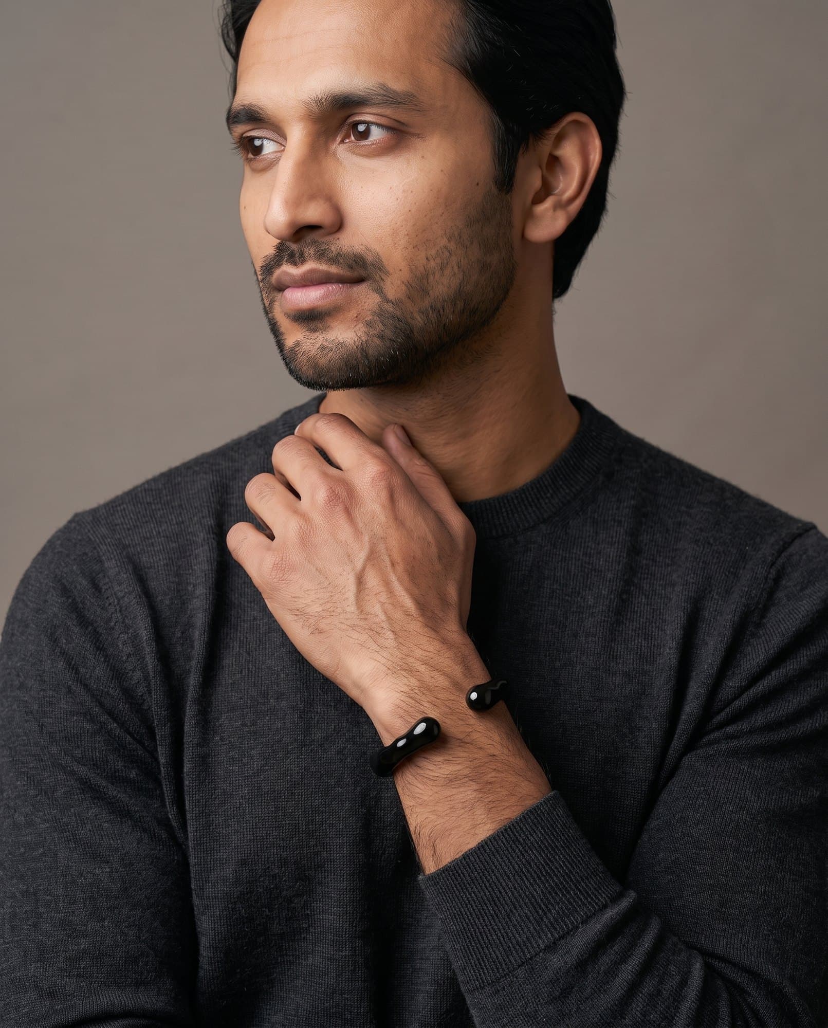 A man in a charcoal knit with his hand at his collarbone, the Onyx Molten Cuff on his wrist.