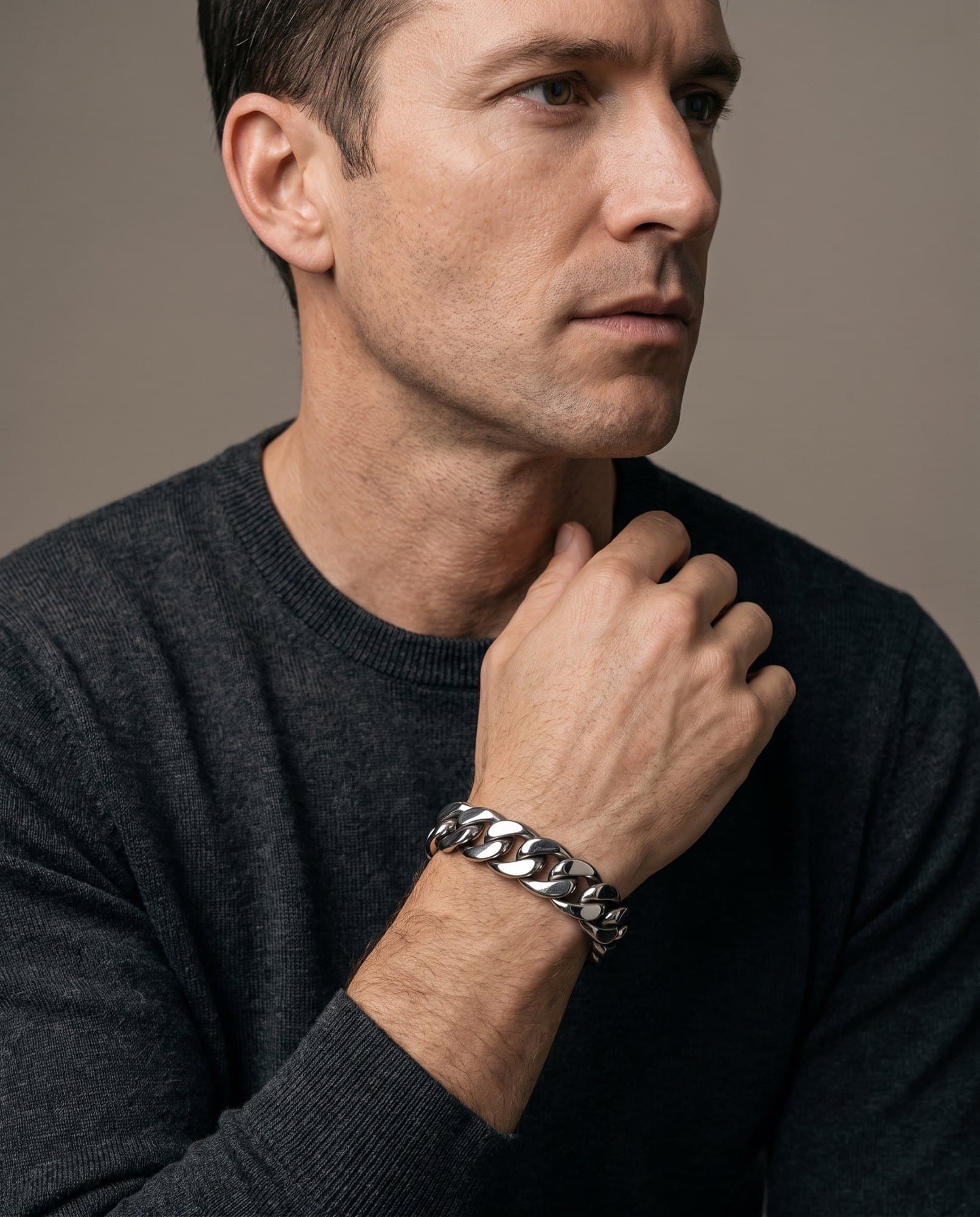 A man in a charcoal knit with his hand at his collarbone, the Pillar Link Cuff on his wrist.