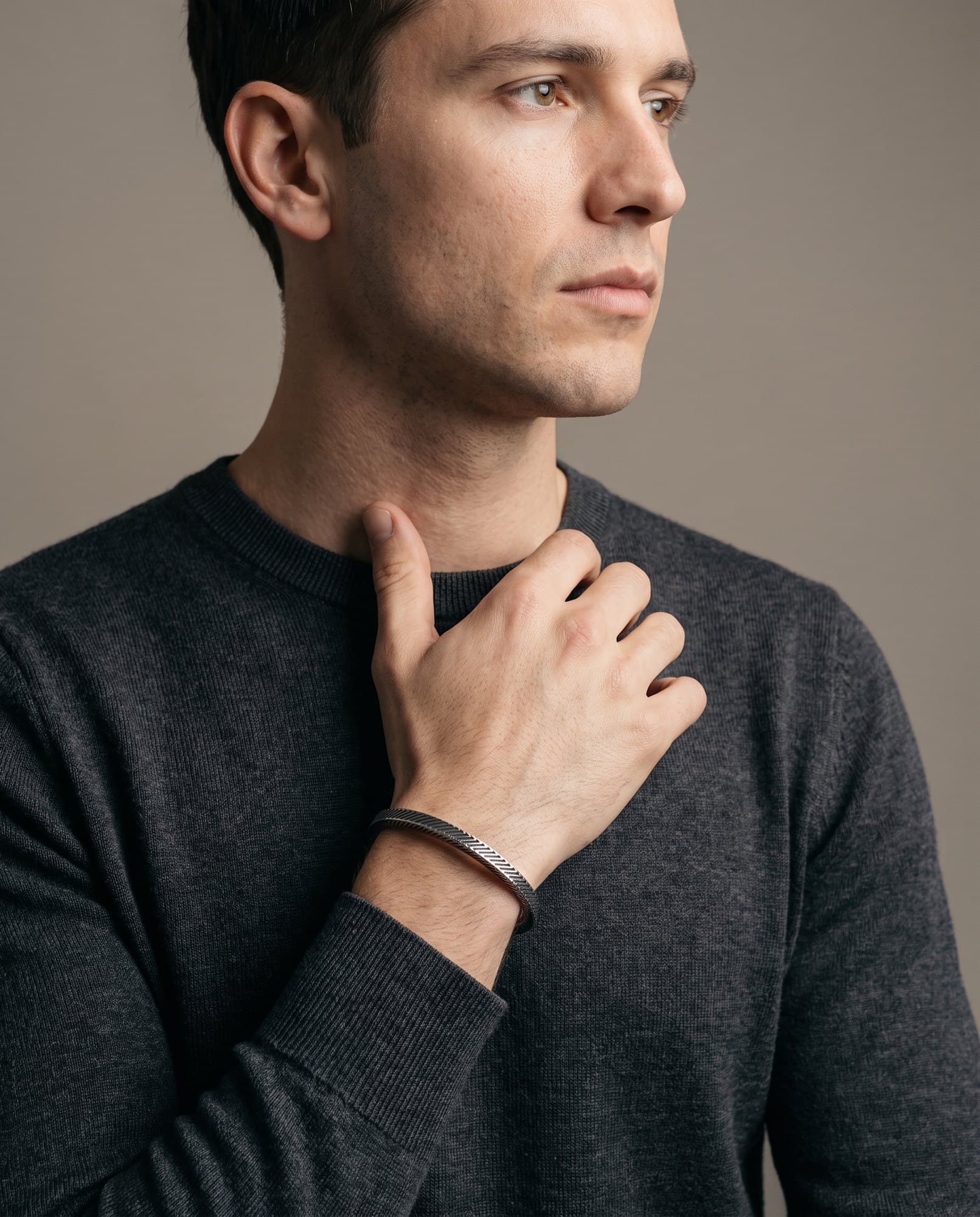 A man in a charcoal knit with his hand at his collarbone, the Regent Cable Cuff on his wrist.
