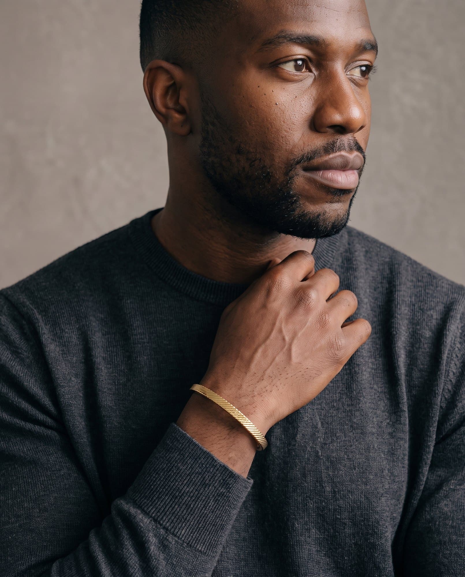 A man in a charcoal knit with his hand at his collarbone, the Regent Reed Cuff on his wrist.