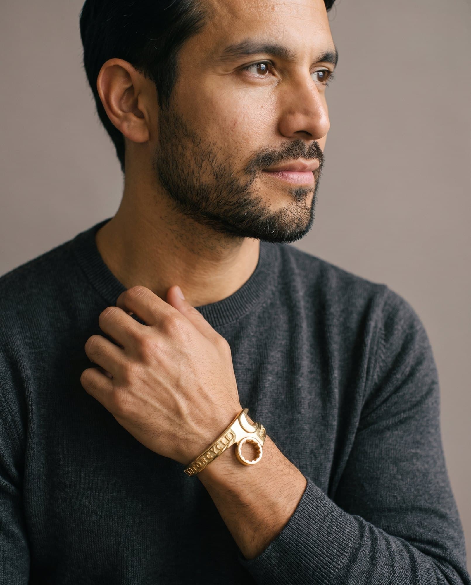 A man in a charcoal knit with his hand at his collarbone, the Regent Wrench Cuff on his wrist.