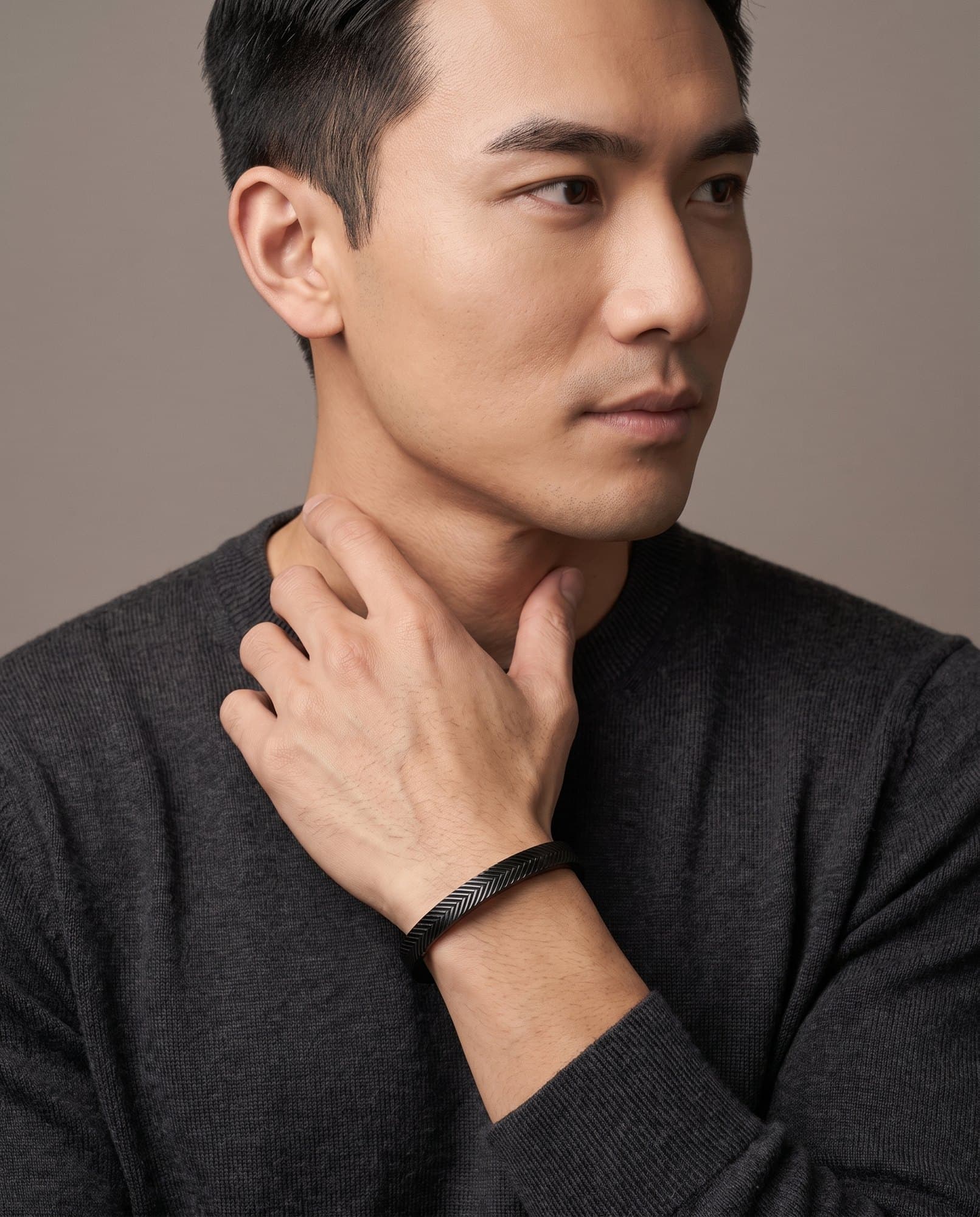 A man in a charcoal knit with his hand at his collarbone, the Sphinx Chevron Cuff on his wrist.