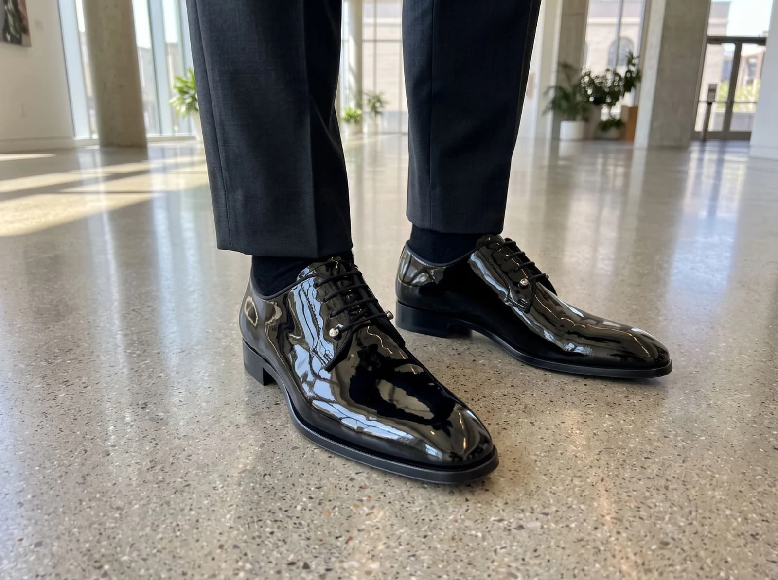 Patent derbys worn with grey trousers and black socks in a bright atrium