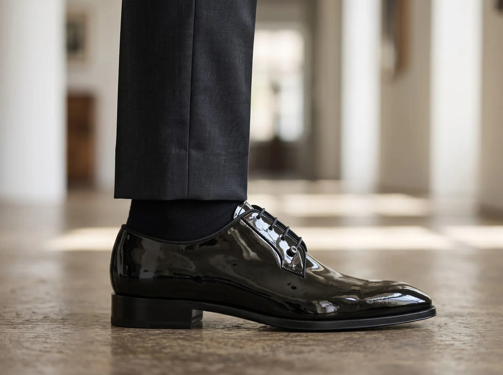 Patent derby in side view, worn with grey trousers and a black sock, the silver bar at the eyelets